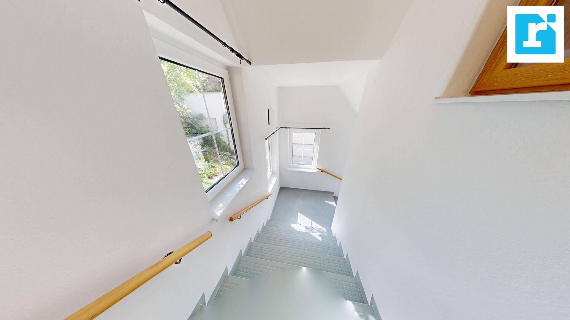 Treppenhaus mit hellgrauen Stufen und großen Fenstern, die viel Licht spenden.