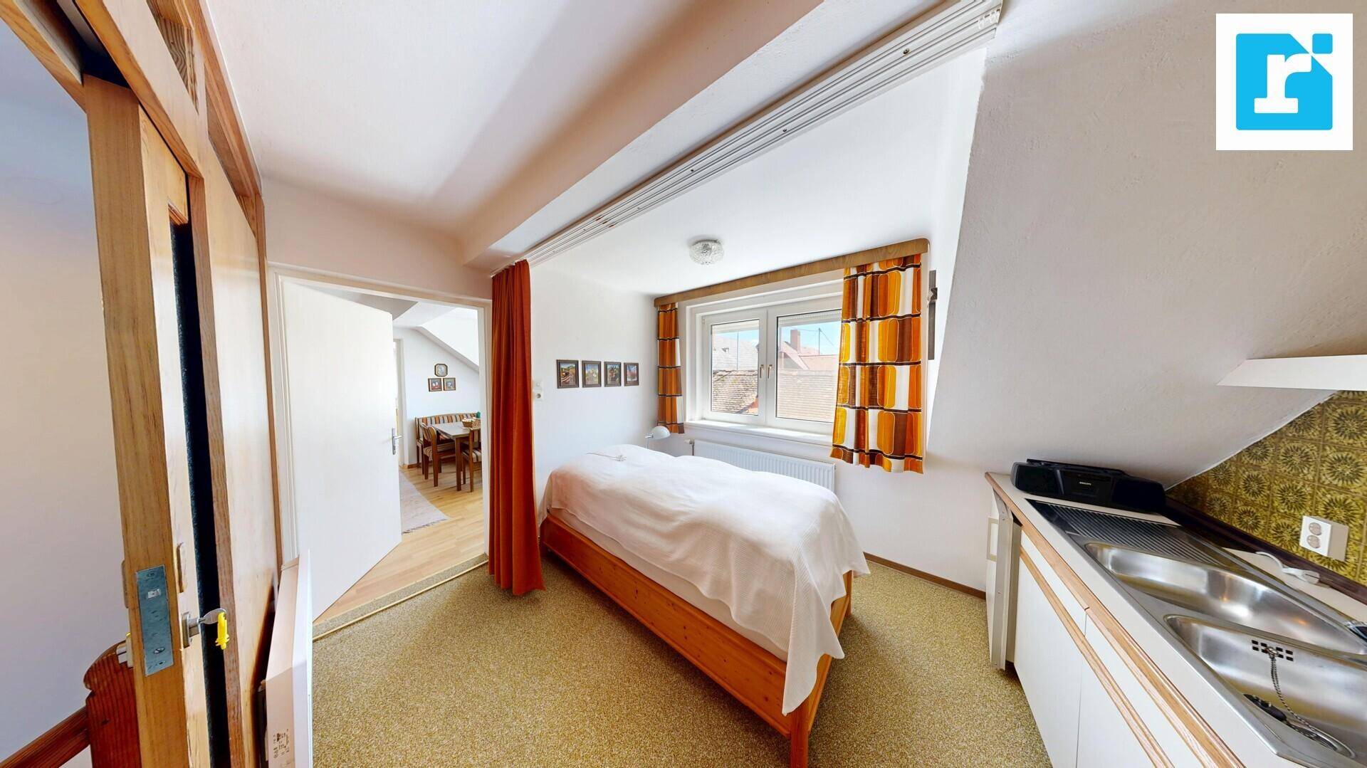 Schlafbereich im Dachgeschoss mit Einzelbett, Fenster und angrenzender kleiner Küchenzeile.