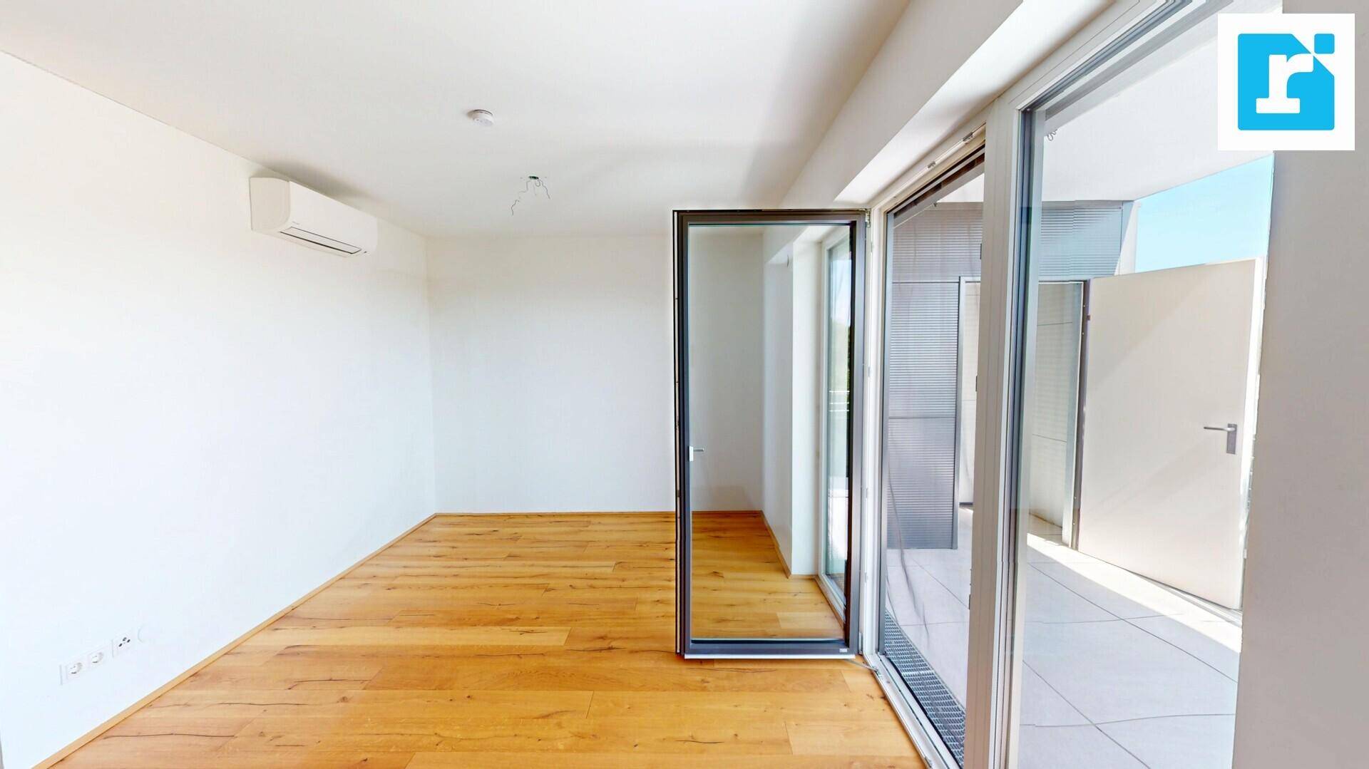 Geräumiges Wohnzimmer mit Holzboden, Klimaanlage und Zugang zu einem Außenbereich.