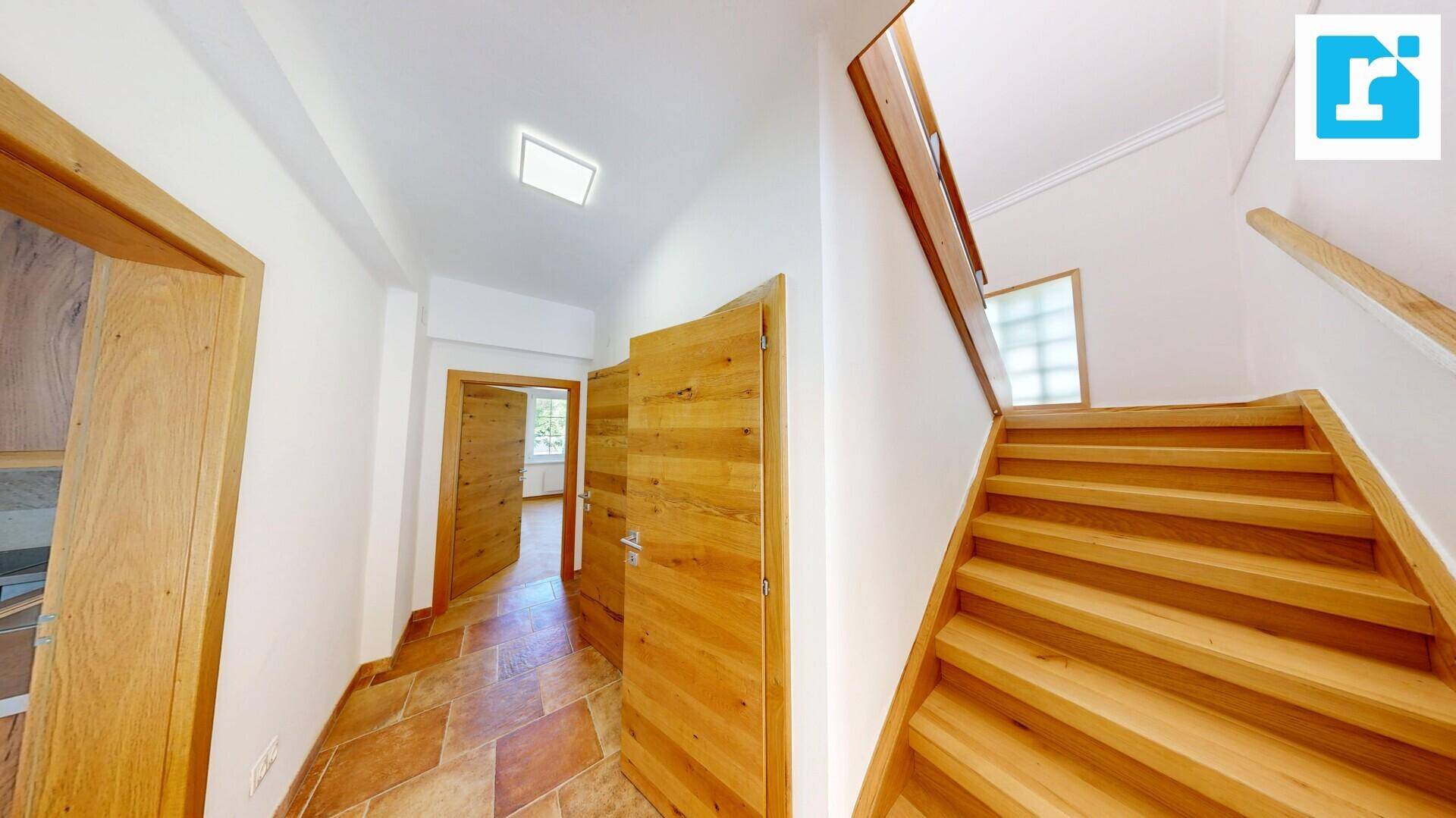 Heller Flur mit Holztüren, gefliestem Boden und einer einladenden Holztreppe.