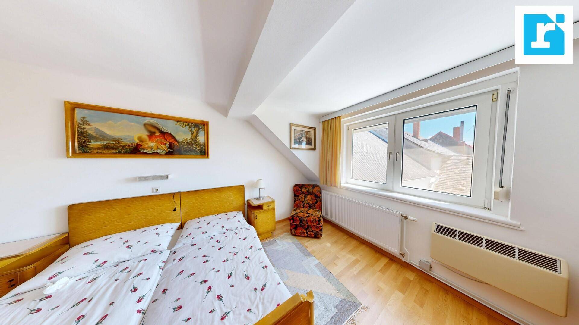 Helles Schlafzimmer im Dachgeschoss mit Doppelbett, Holzboden und Fenster mit Blick nach draußen.
