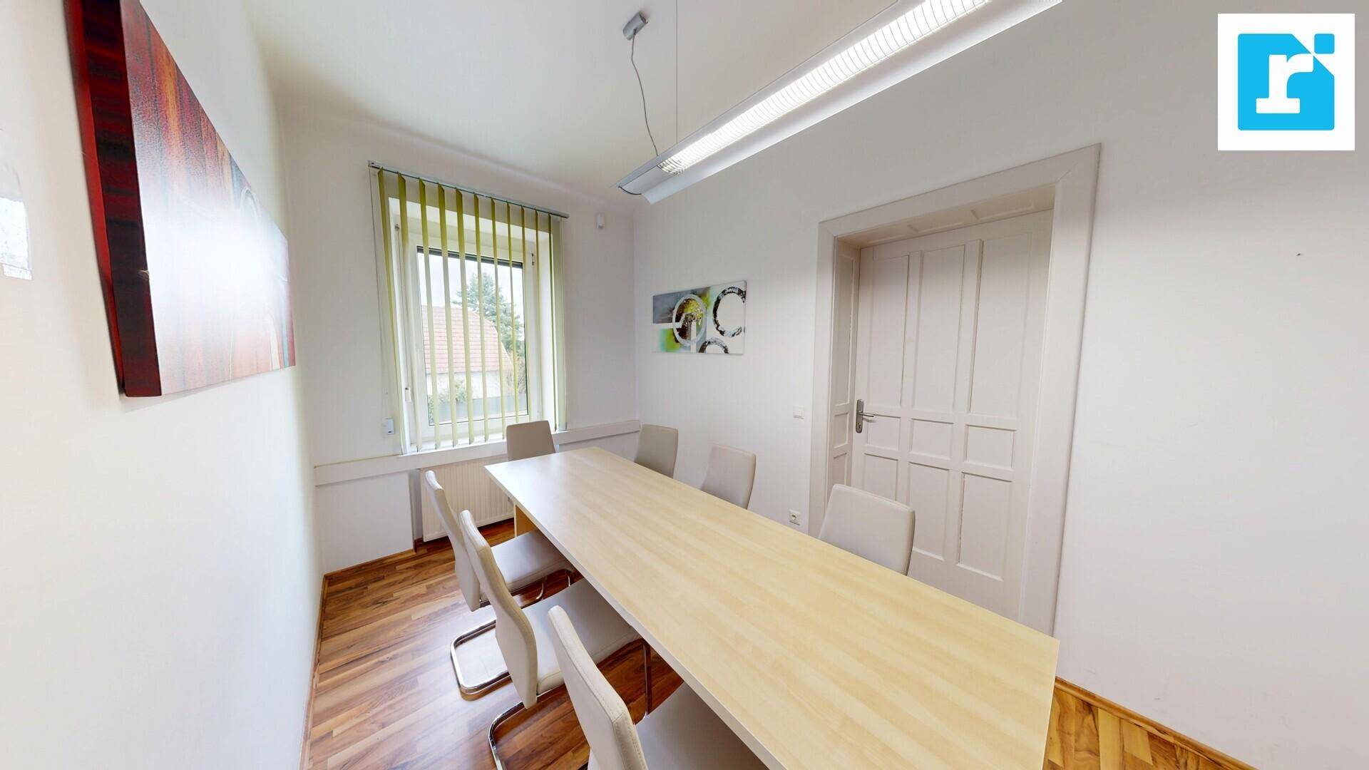 Besprechungsraum mit einem langen Holztisch, bequemen Stühlen und einem Fenster mit Jalousien für Privatsphäre.