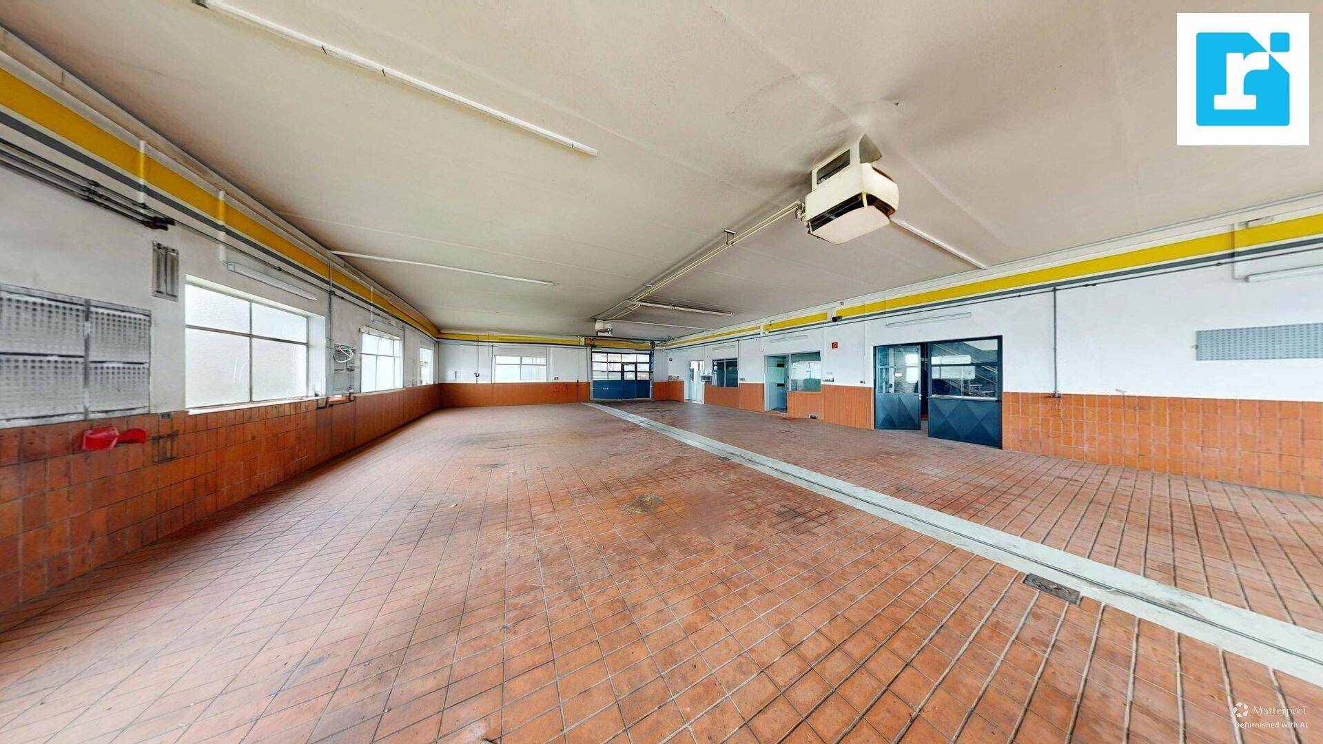 Geräumige Werkstatt mit Terrakotta-Fliesenboden und hohen Decken, gut beleuchtet.