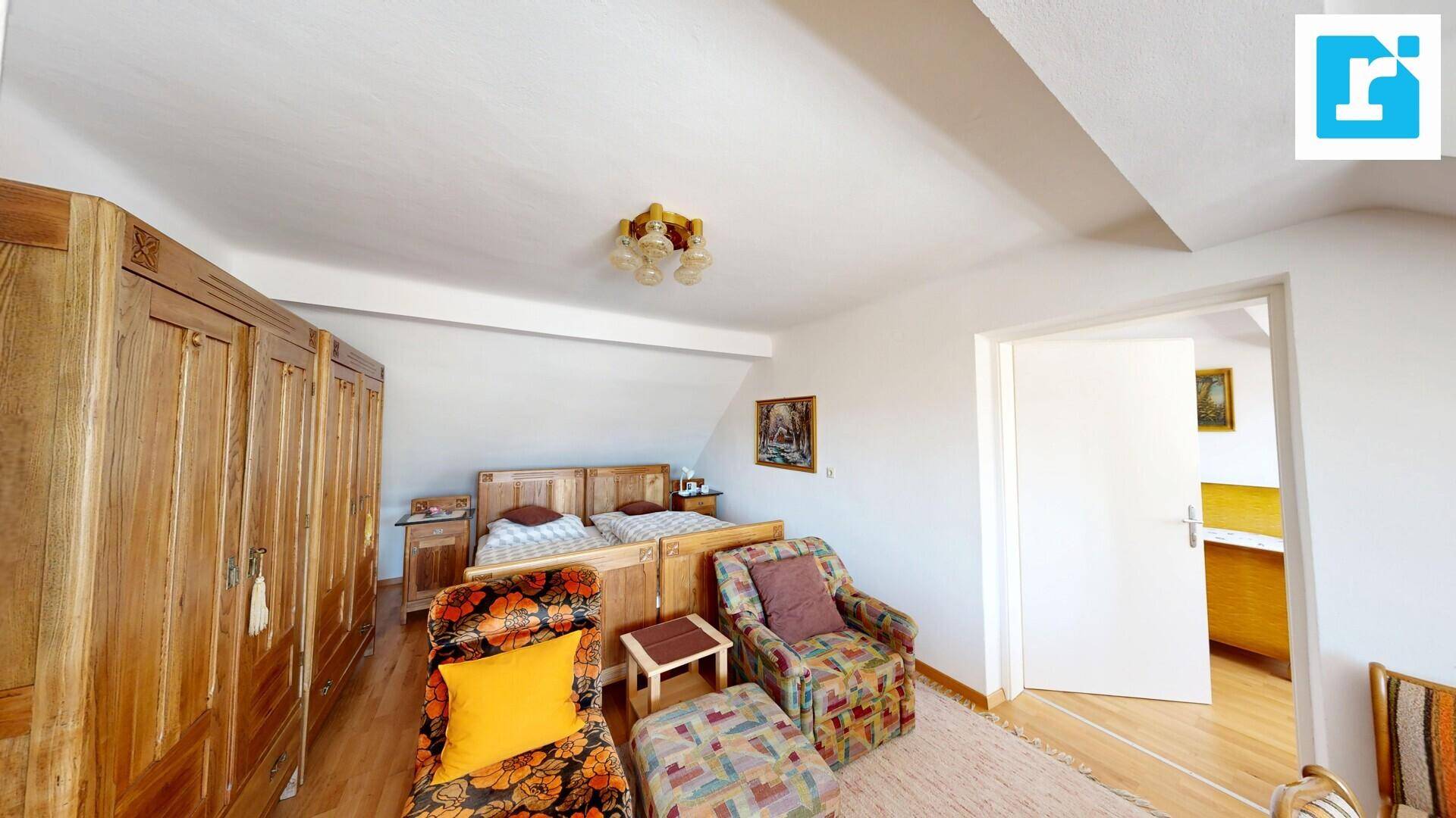 Schlafzimmer im Dachgeschoss mit Doppelbett, Holzschrank und bequemen Sesseln.