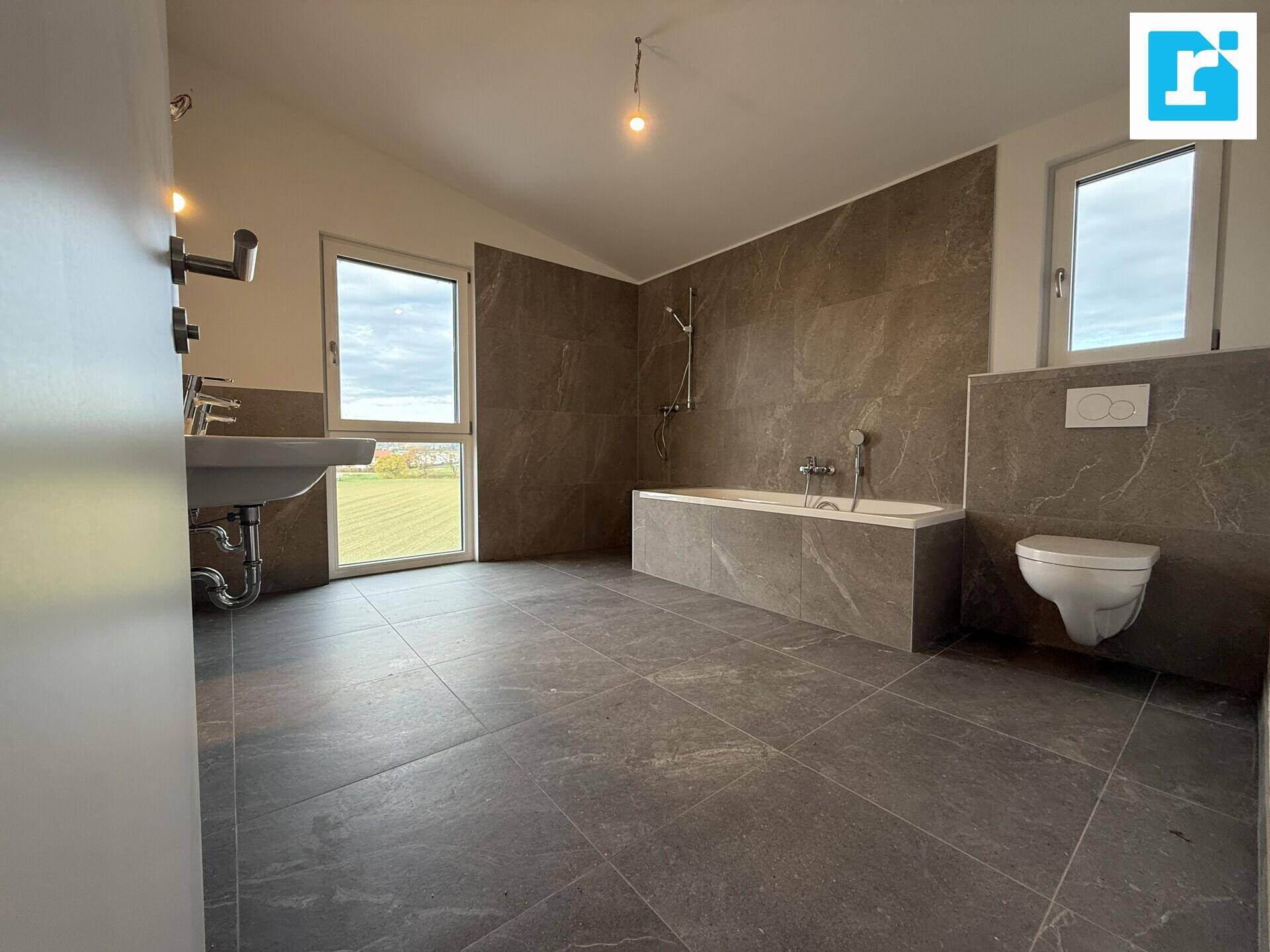 Modernes Badezimmer mit Badewanne, WC und Fenster für natürliche Belichtung.