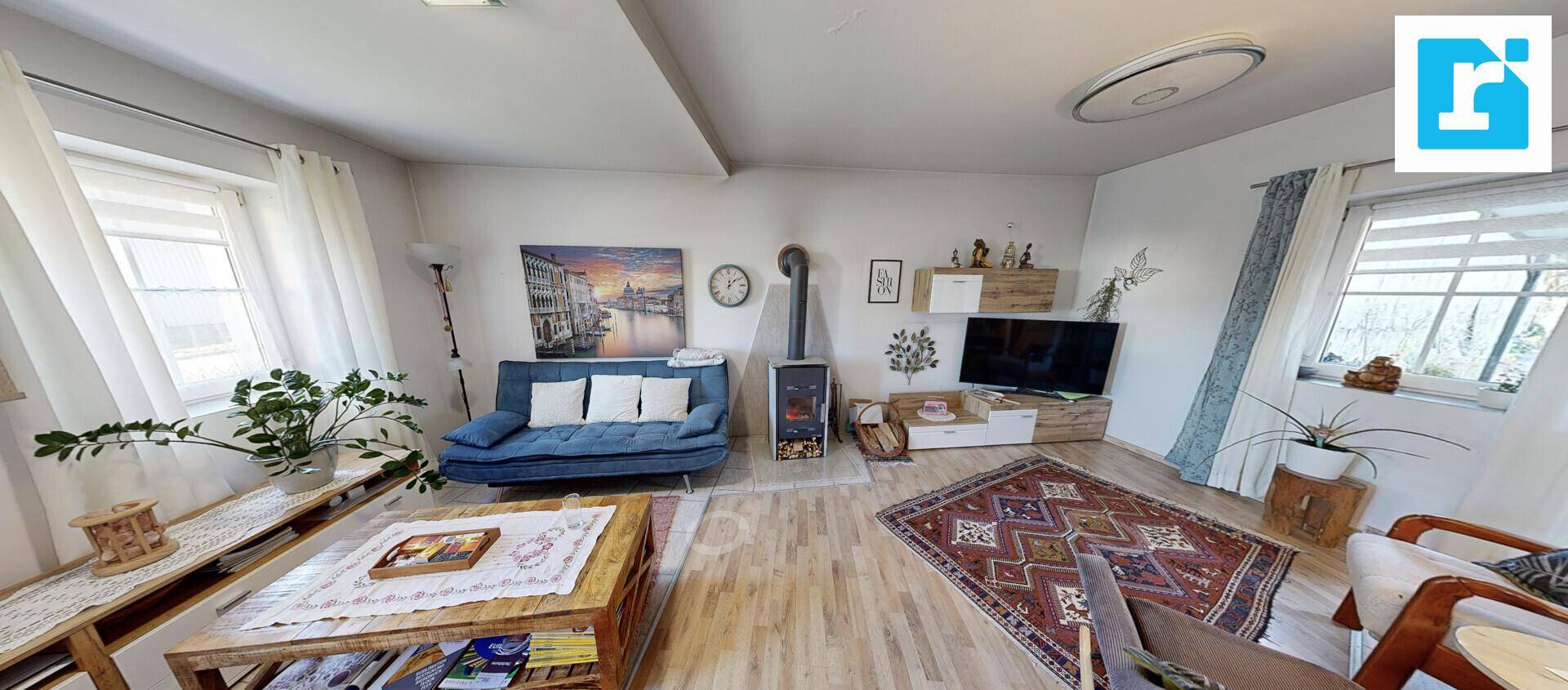 Wohnzimmer mit blauem Sofa, Couchtisch und einem gemütlichen Holzofen.
