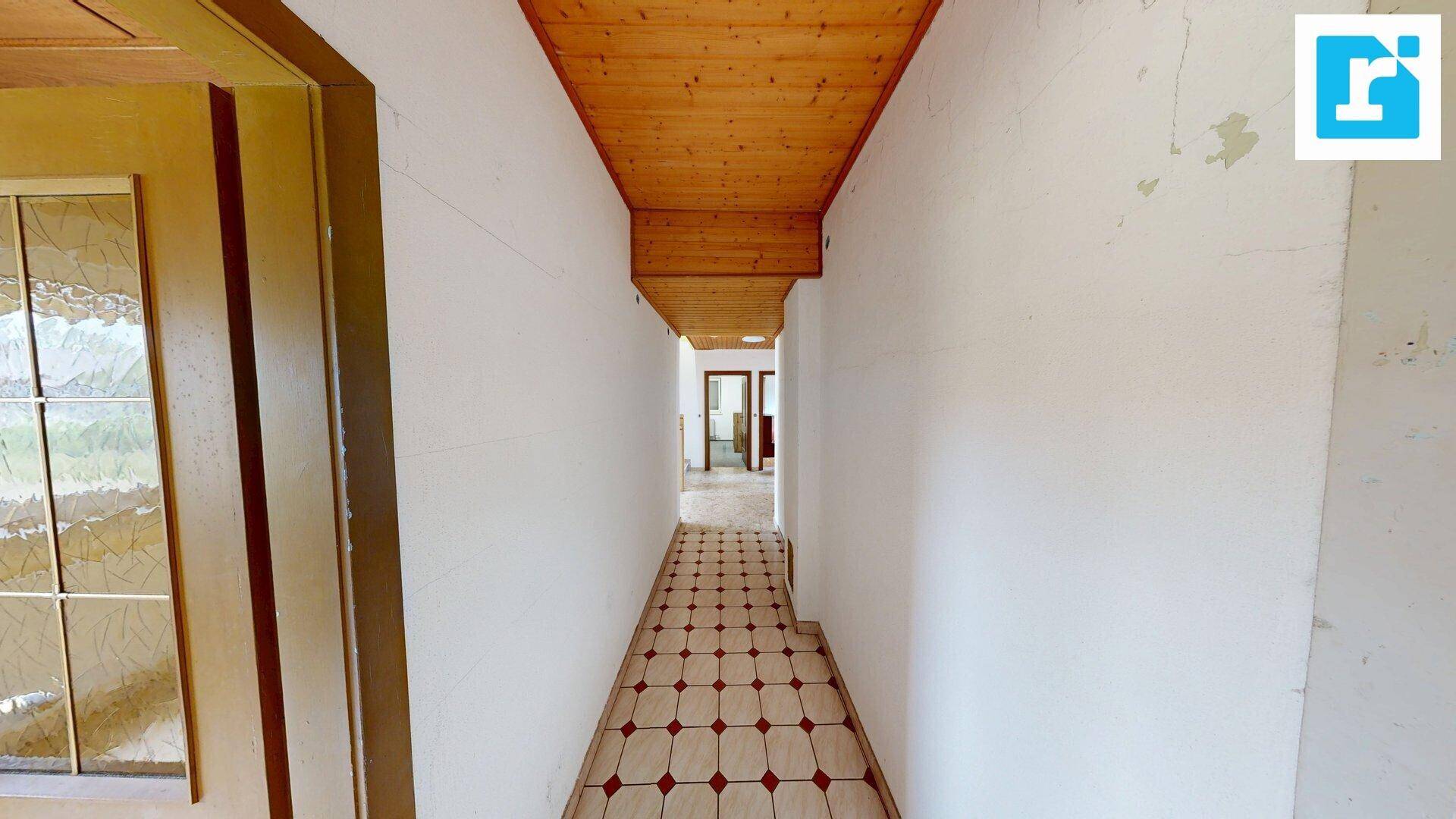 Langer Flur mit gemusterten Fliesen und Holzdecke, führt zu weiteren Räumen.