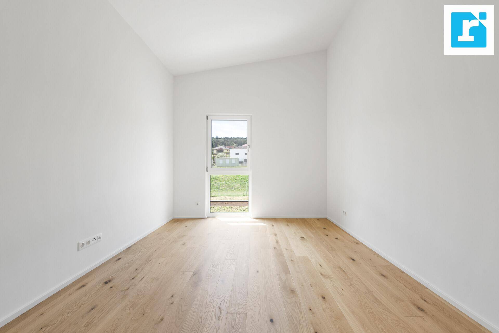 Helles Zimmer mit Holzboden, schräger Decke und Fenster mit Blick ins Grüne.