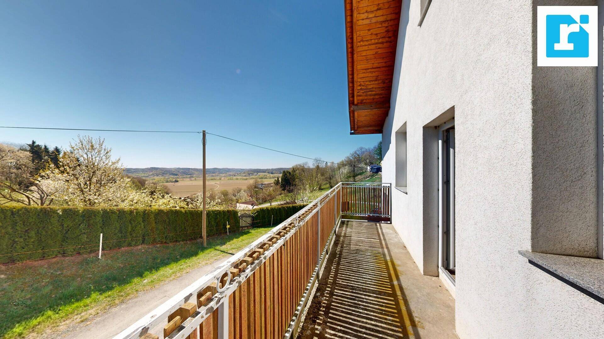 Balkon mit Holzgeländer und weitem Blick über die grüne Landschaft.