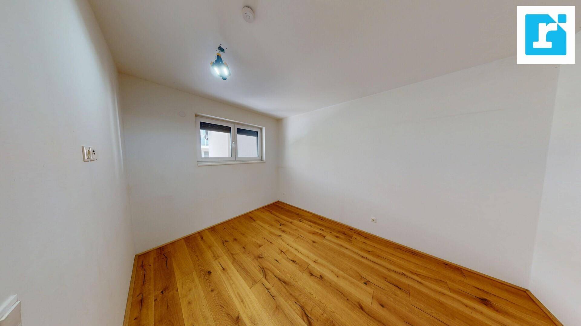 Kleines Zimmer mit Holzboden und einem Fenster, ideal als Schlaf- oder Arbeitszimmer.