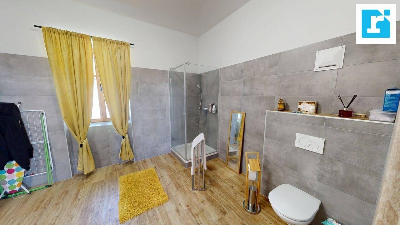 Modernes Badezimmer mit grauen Fliesen, Holzboden, Duschkabine und WC, hell durch das Fenster.
