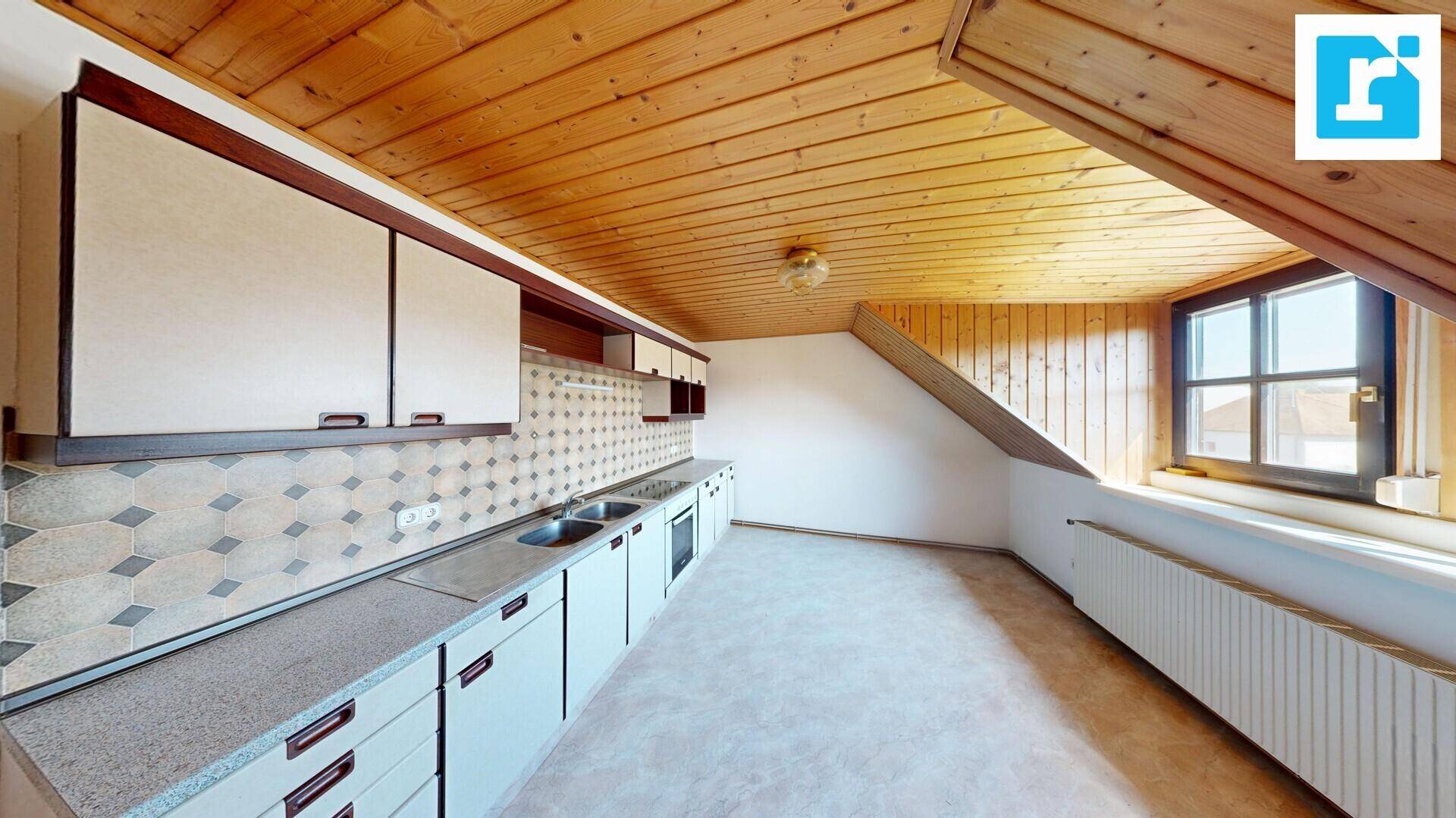 Dachgeschossküche mit Holzdecke, weißen Schränken und einem Fenster.