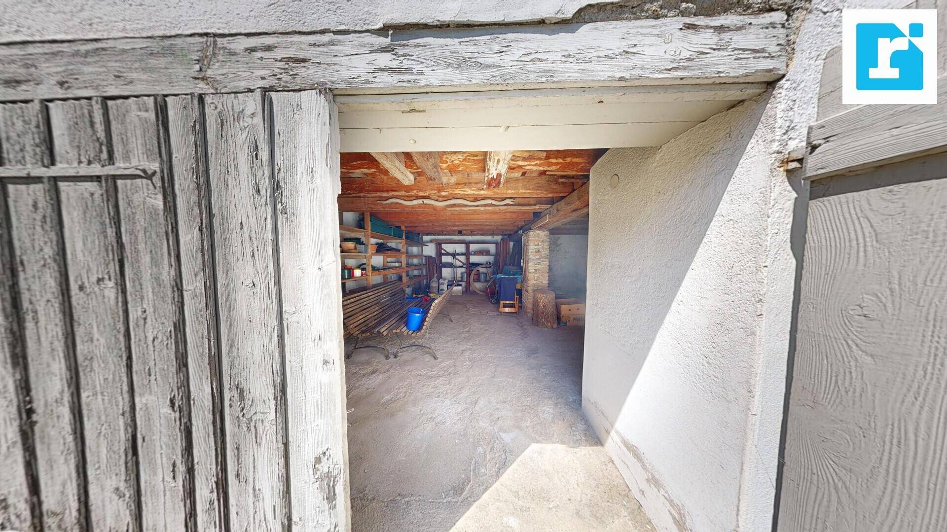 Rustikaler Lagerraum mit Holzbalken an der Decke und Betonboden, durch eine Holztür zugänglich.