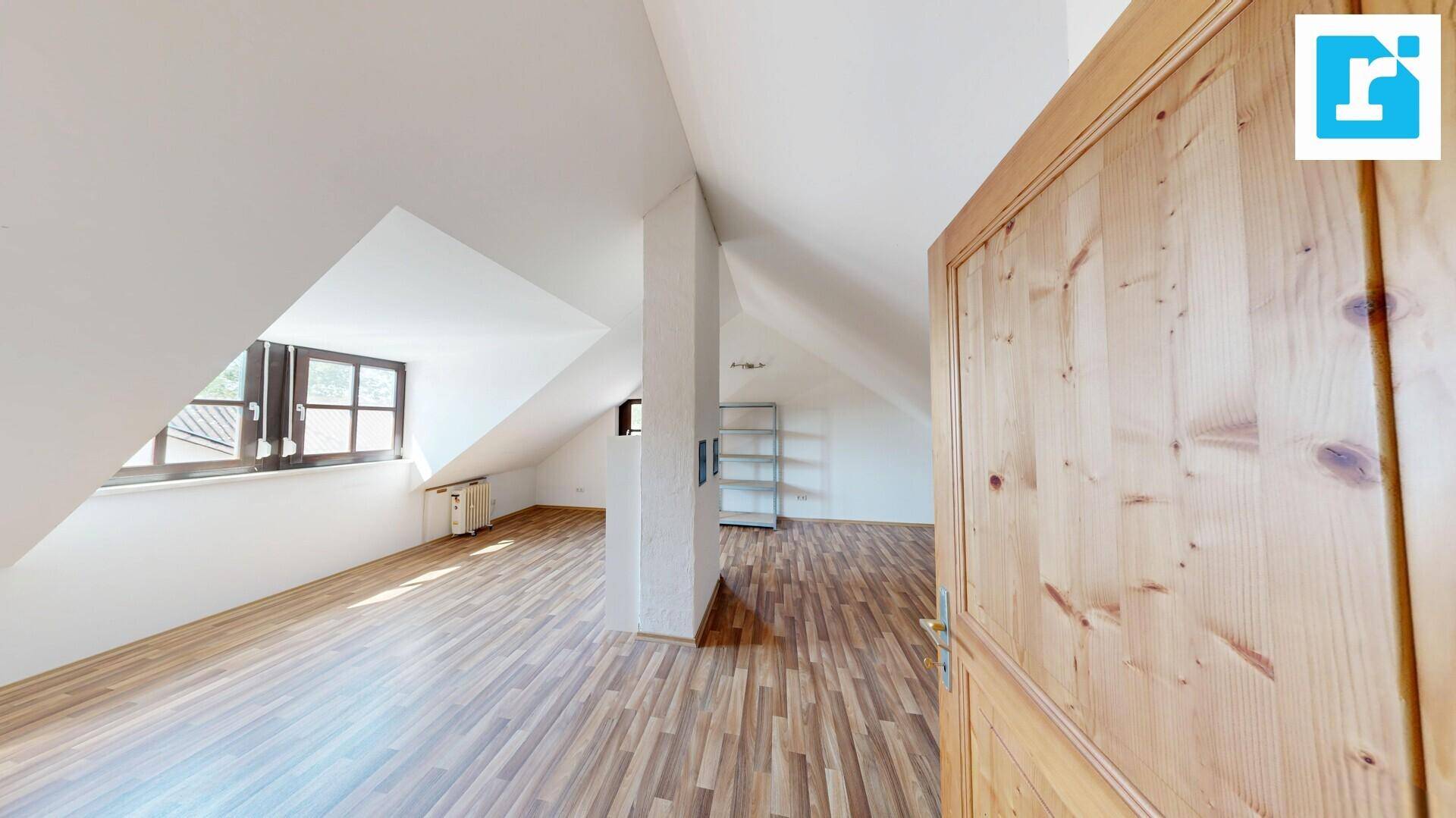 Helles Dachzimmer mit schrägen Wänden, Laminatboden und einem Fenster.