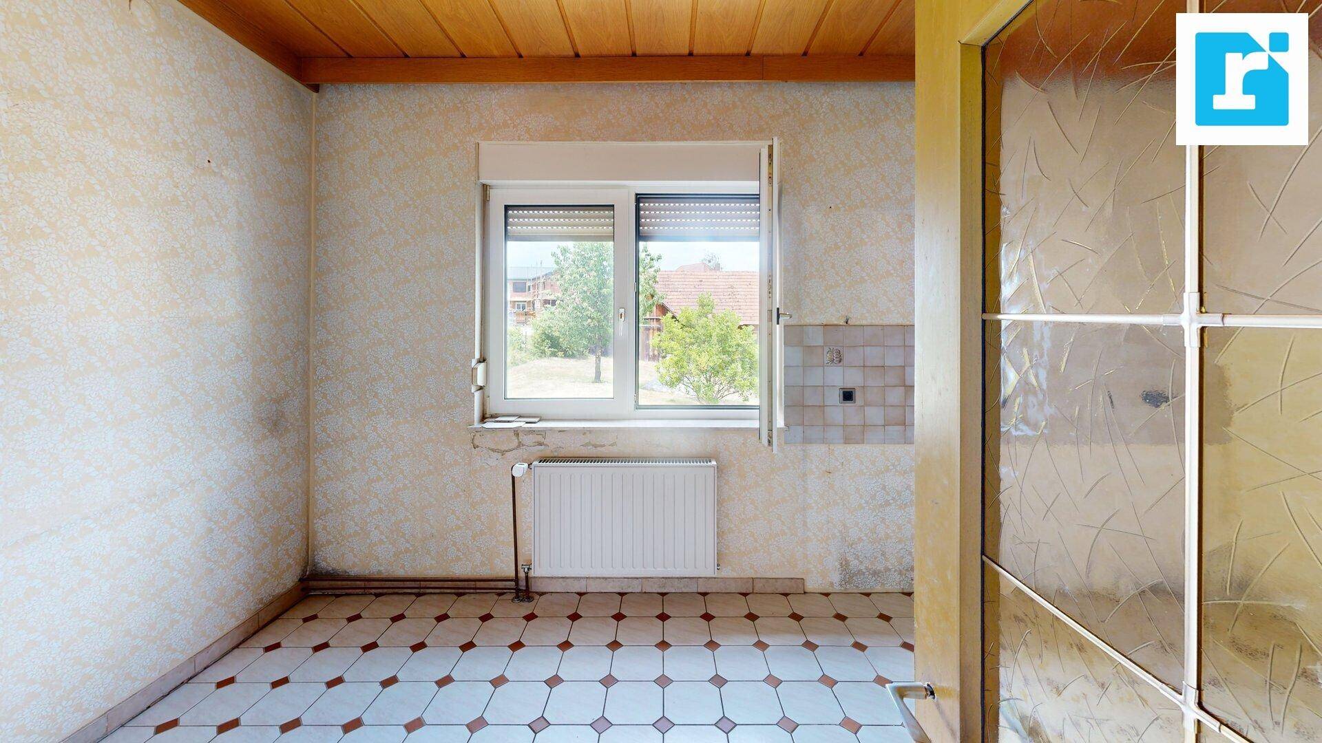Leere Küche mit gemusterten Fliesen und Holzdecke, bereit für eine neue Einrichtung.