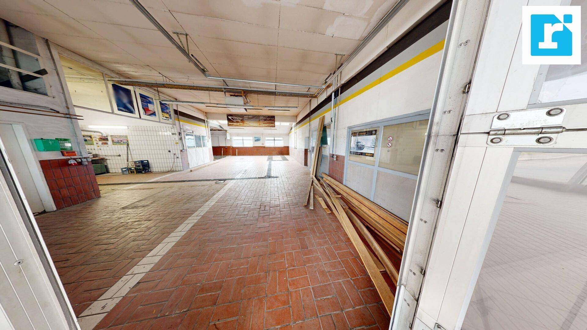 Werkstatt mit Terrakotta-Fliesenboden und Zugang zu Garagentoren, ideal für Fahrzeugservice.