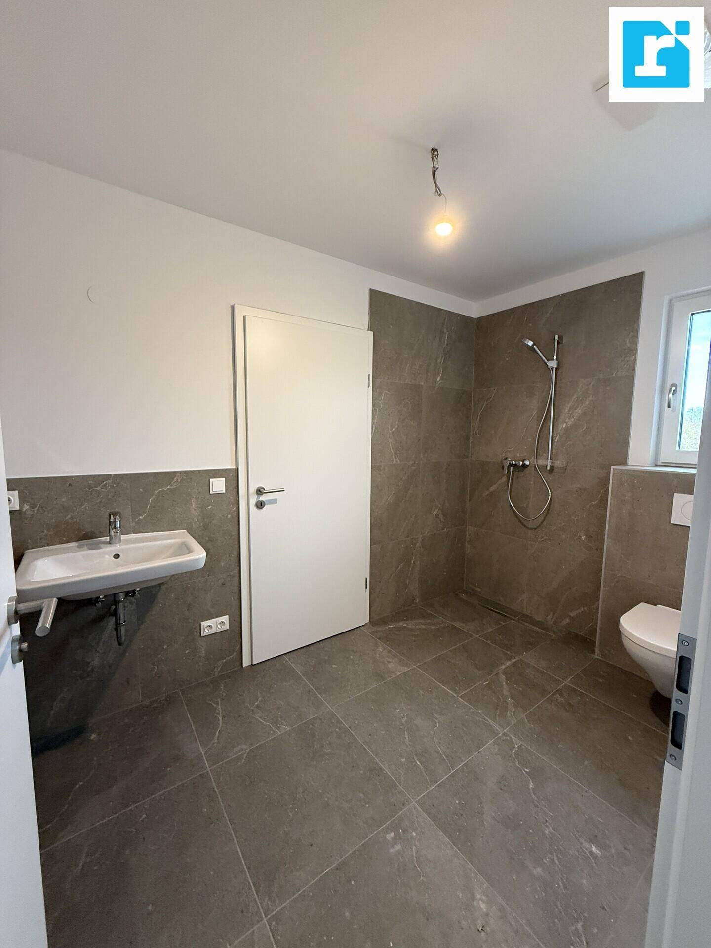 Modernes Badezimmer mit Dusche, Waschbecken und grauen Fliesen.