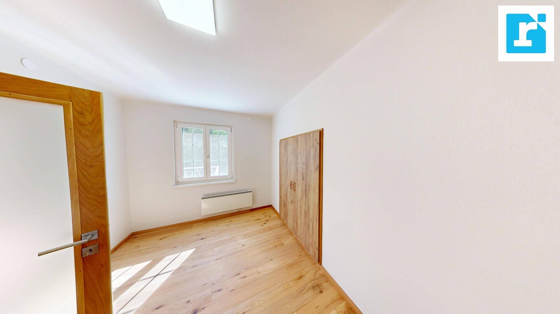 Freundliches Schlafzimmer mit Holzdielenboden, Fenster und integriertem Kleiderschrank.