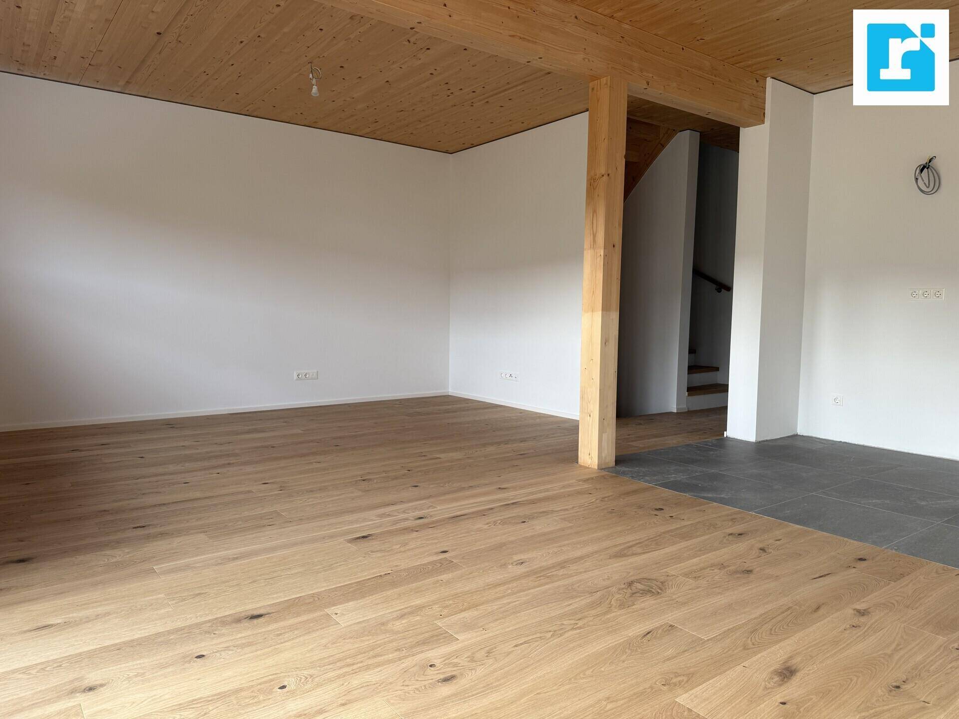 Heller Wohnbereich mit Holzbalkendecke, Parkett und Treppenaufgang.