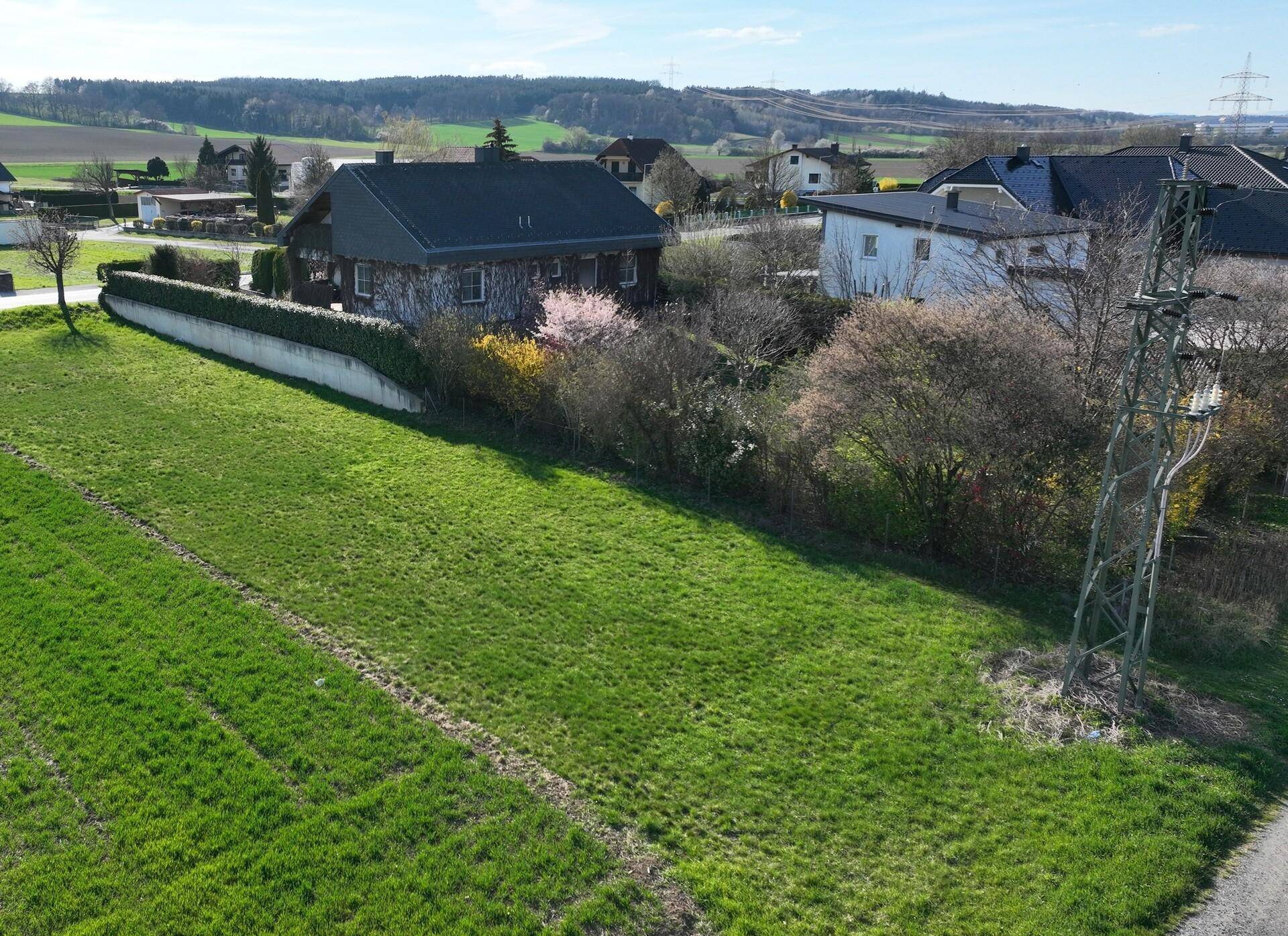 Blick aus der Vogelperspektive auf ein Wohnhaus mit gepflegtem Garten und weiten Feldern im Hintergrund.