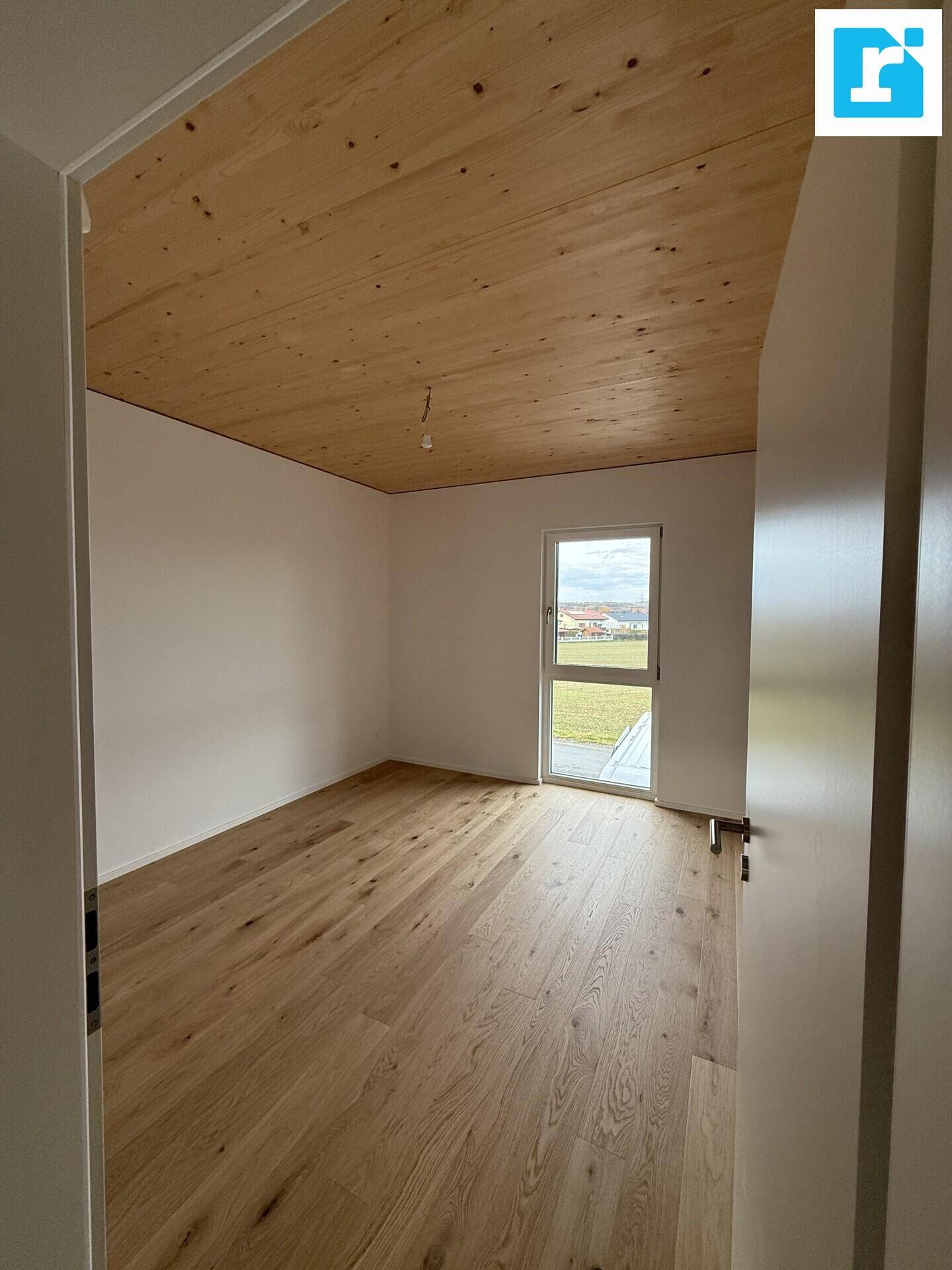 Helles Schlafzimmer mit Holzbalkendecke, Parkettboden und Zugang nach draußen.