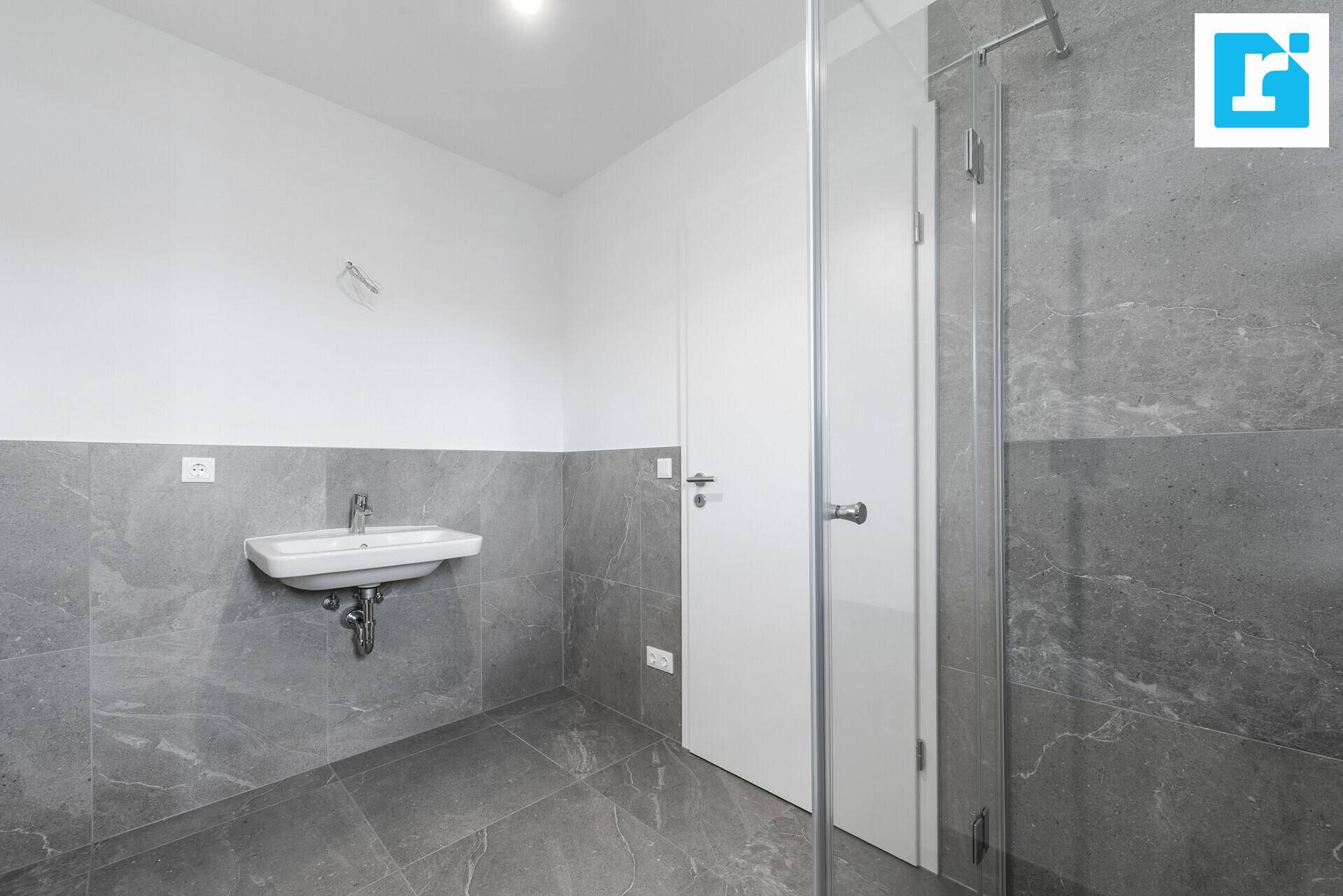 Modernes Badezimmer mit Waschbecken, Duschbereich und grauen Fliesen.