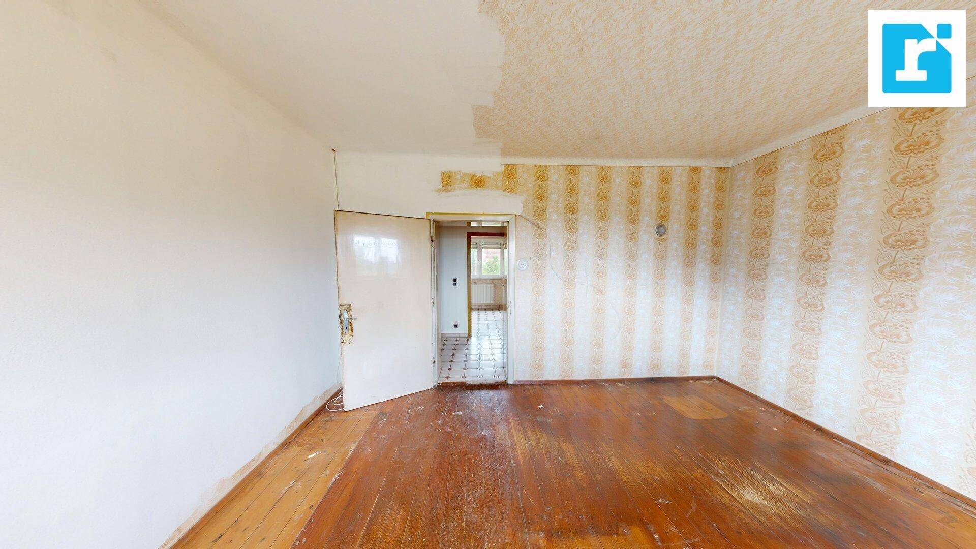 Geräumiges Zimmer mit Holzboden und alter Tapete, bereit für eine Renovierung.
