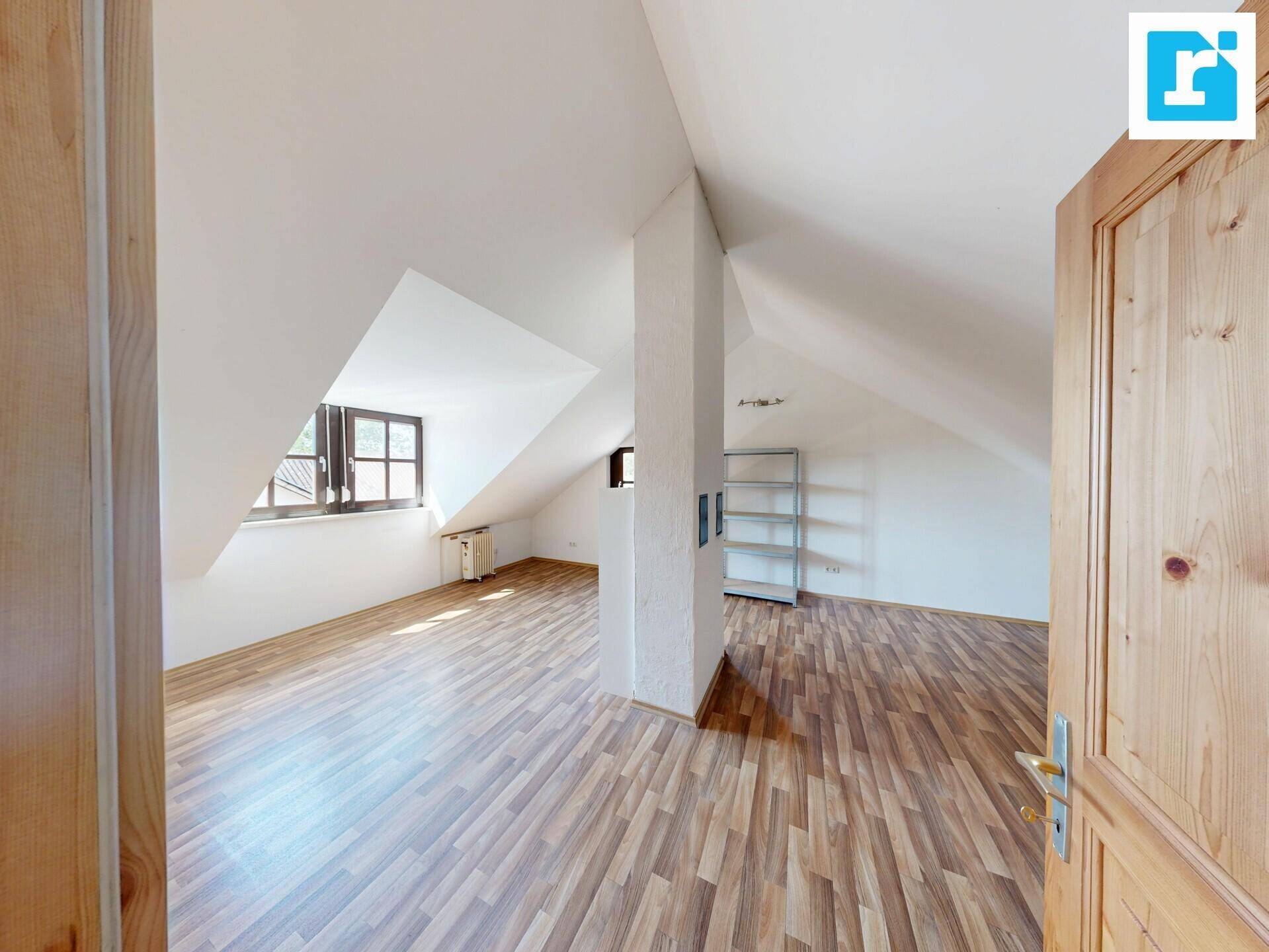 Geräumiges Dachzimmer mit schrägen Wänden, Laminatboden und einem Fenster.