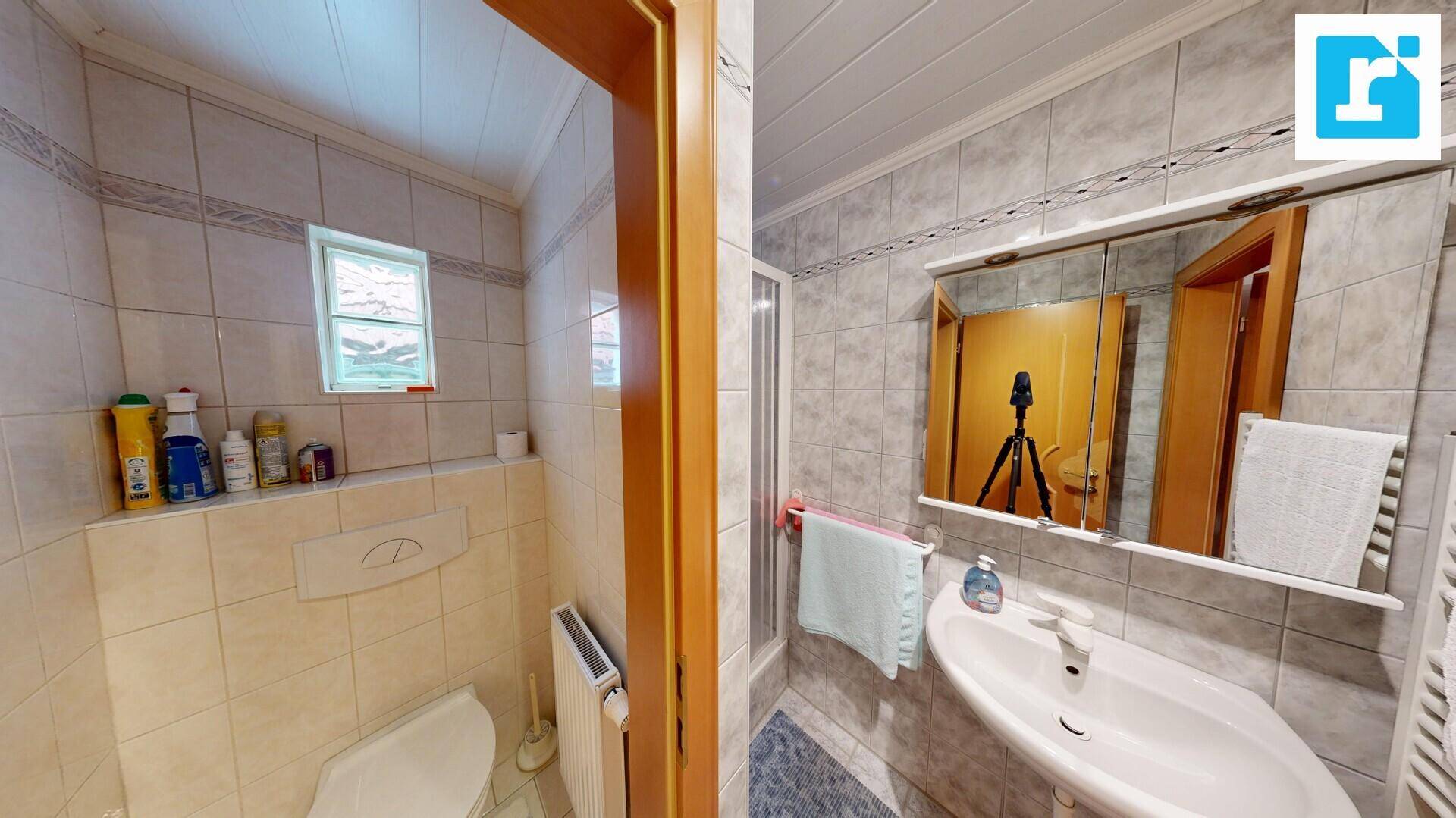 Badezimmer mit Dusche, Waschbecken und separatem WC-Bereich mit Fenster.