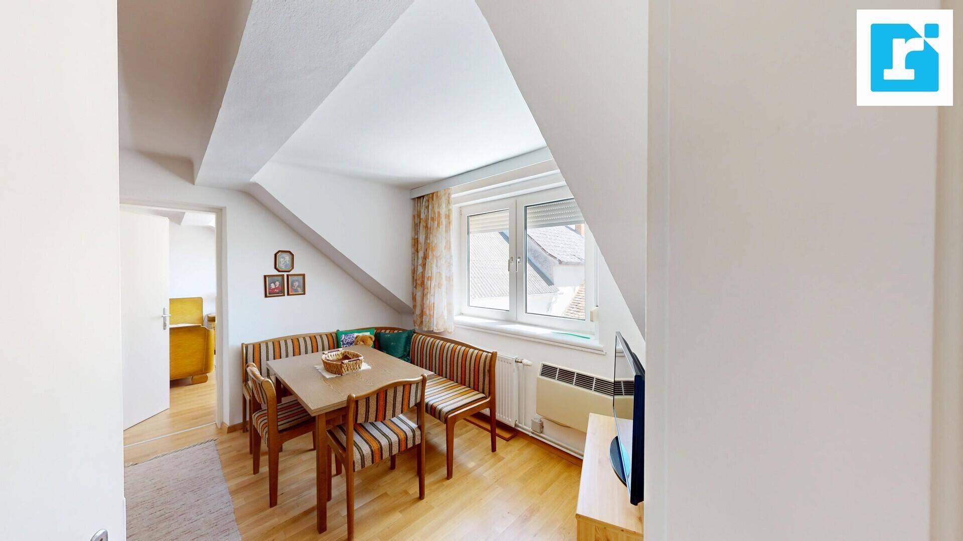 Gemütlicher Essbereich im Dachgeschoss mit Holztisch, Eckbank und Fenster mit Ausblick.