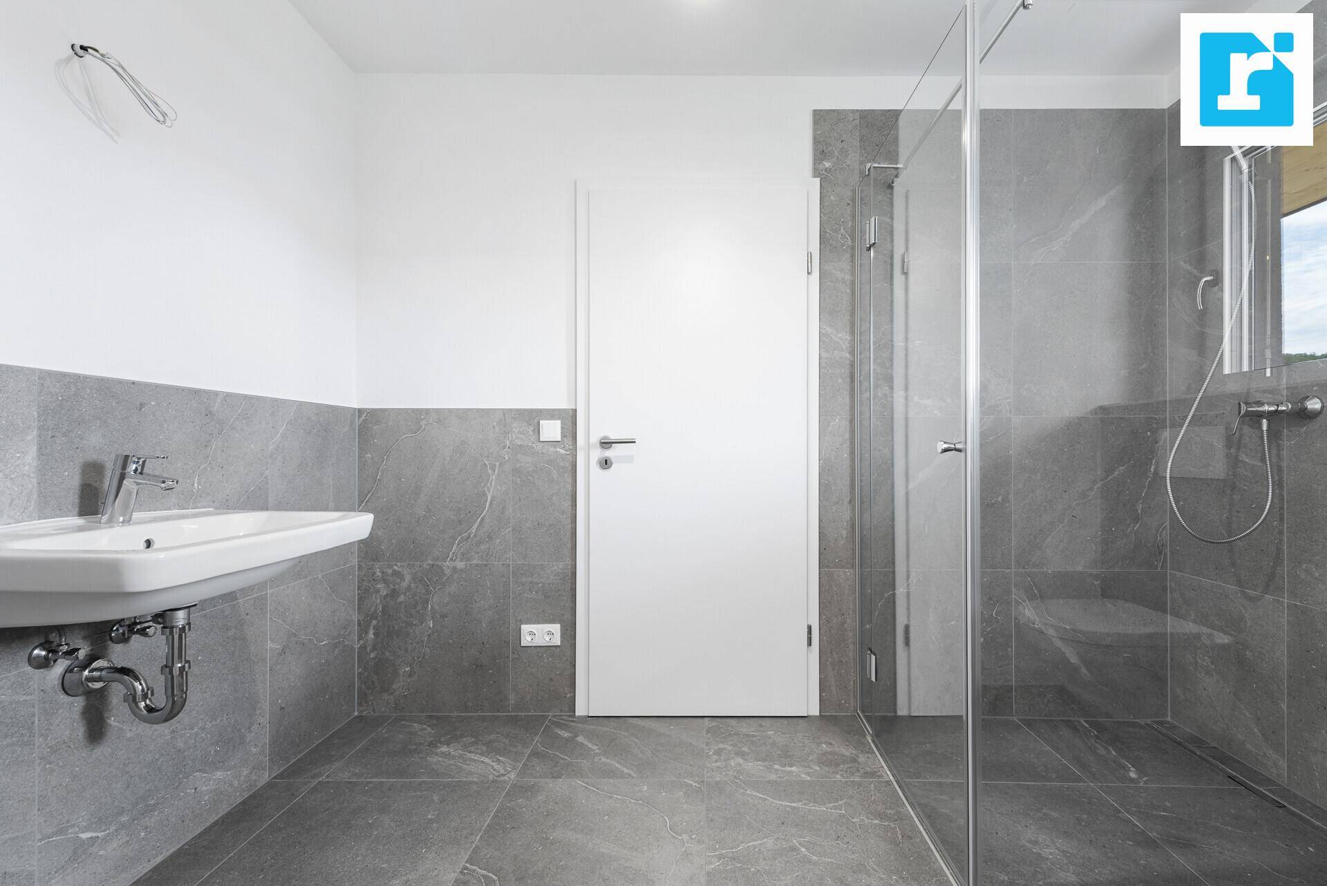 Helles Badezimmer mit Waschbecken, Duschkabine und modernen grauen Fliesen.