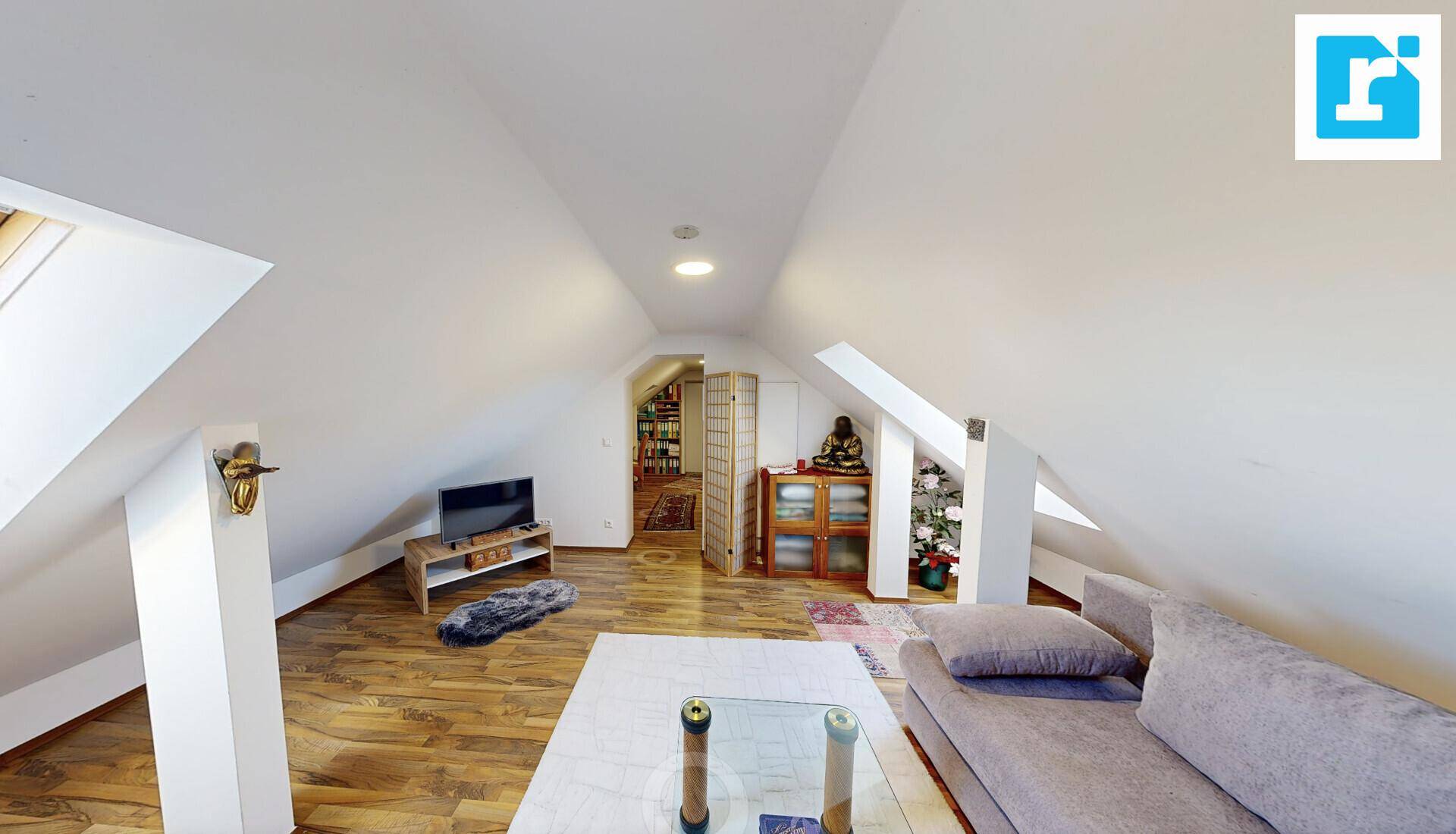 Geräumiger Dachbodenbereich mit schrägen Decken, Sofa und Fernseher.