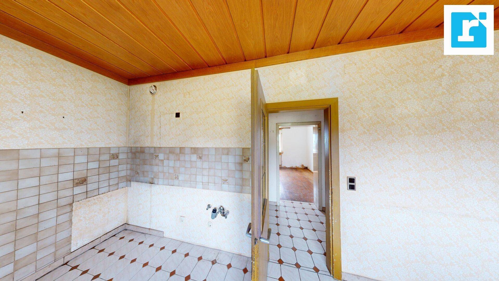 Unmöblierte Küche mit Fliesenboden und Holzdecke, bietet Potenzial zur Gestaltung.