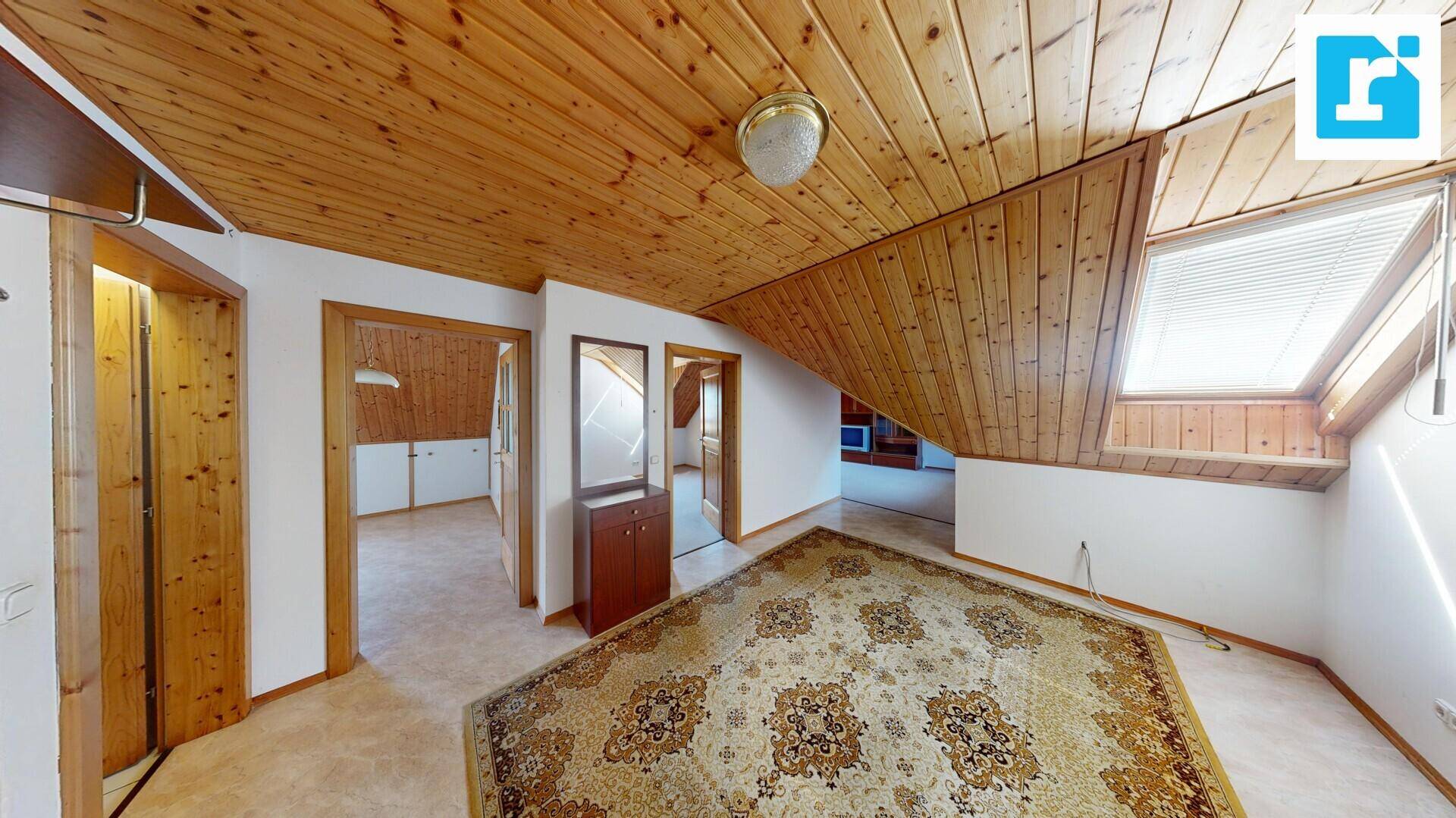 Dachzimmer mit schräger Holzdecke, Dachfenster und Teppichboden.