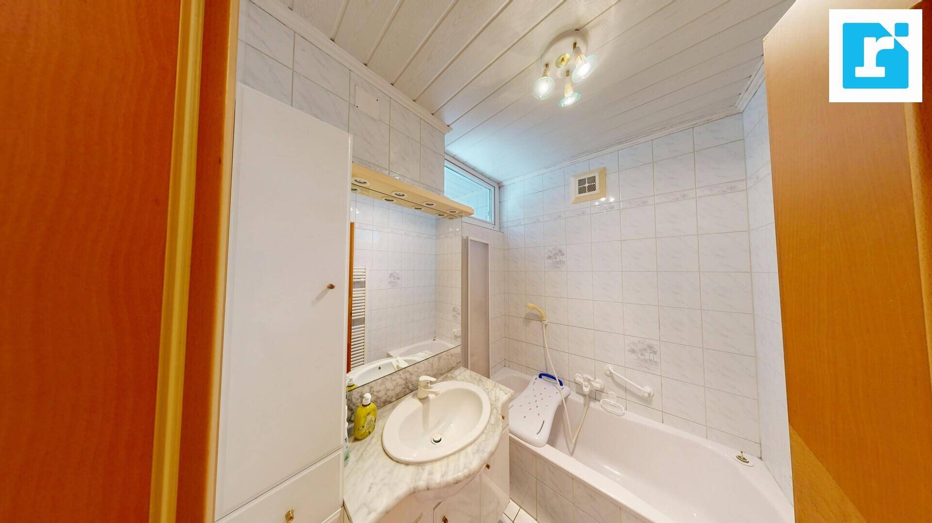 Badezimmer mit Badewanne, Waschbecken und weißen Fliesen an Wänden und Decke.
