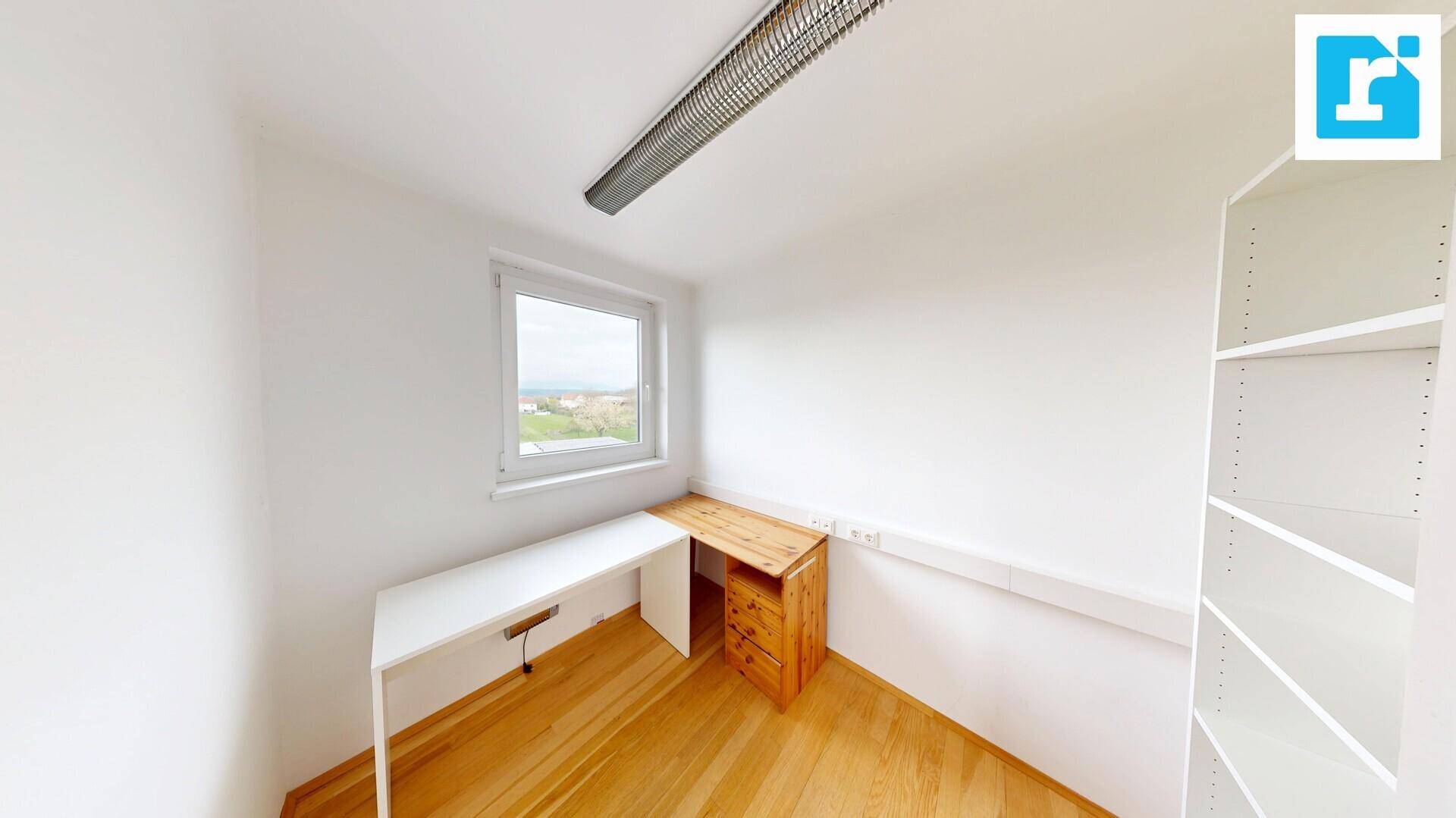 Kleines Büro mit Holzboden, einem Schreibtisch und einem Fenster mit Blick ins Grüne, ideal für konzentriertes Arbeiten.