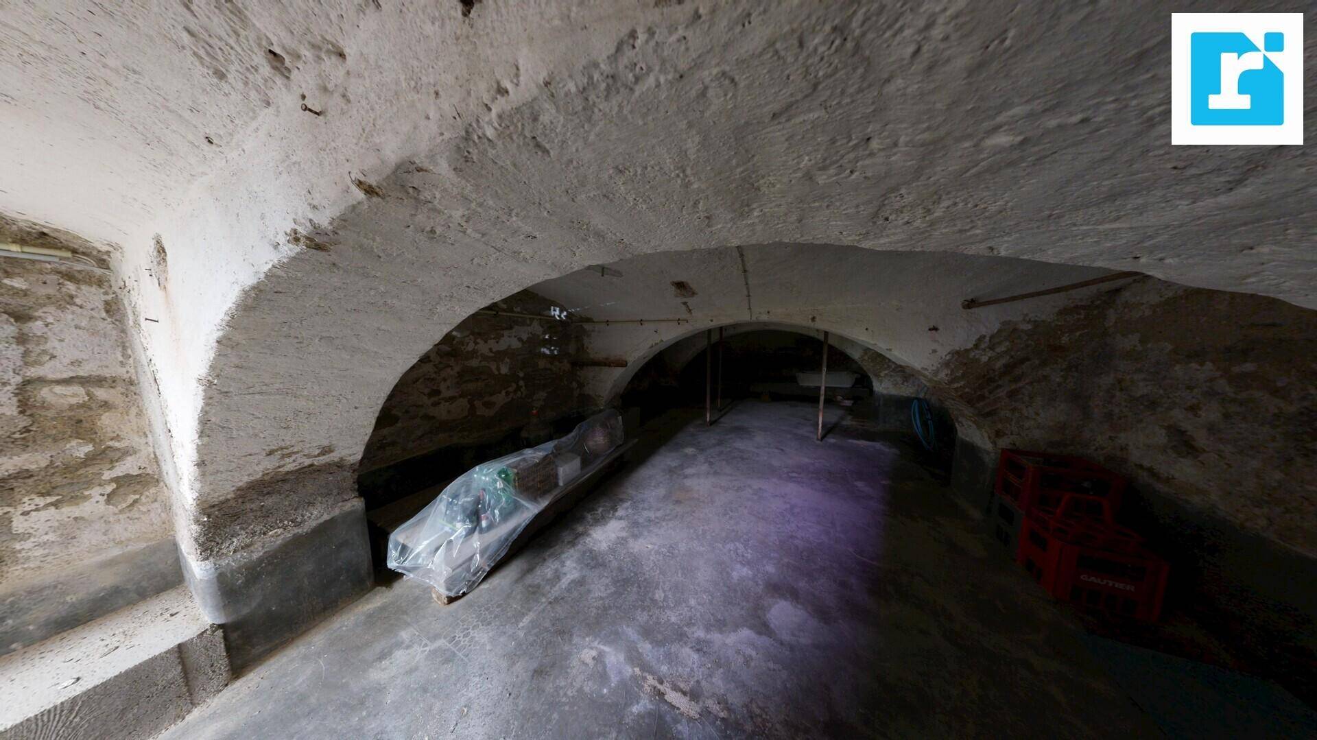 Historischer Gewölbekeller mit robusten Steinmauern und Betonboden, ideal zur Lagerung.