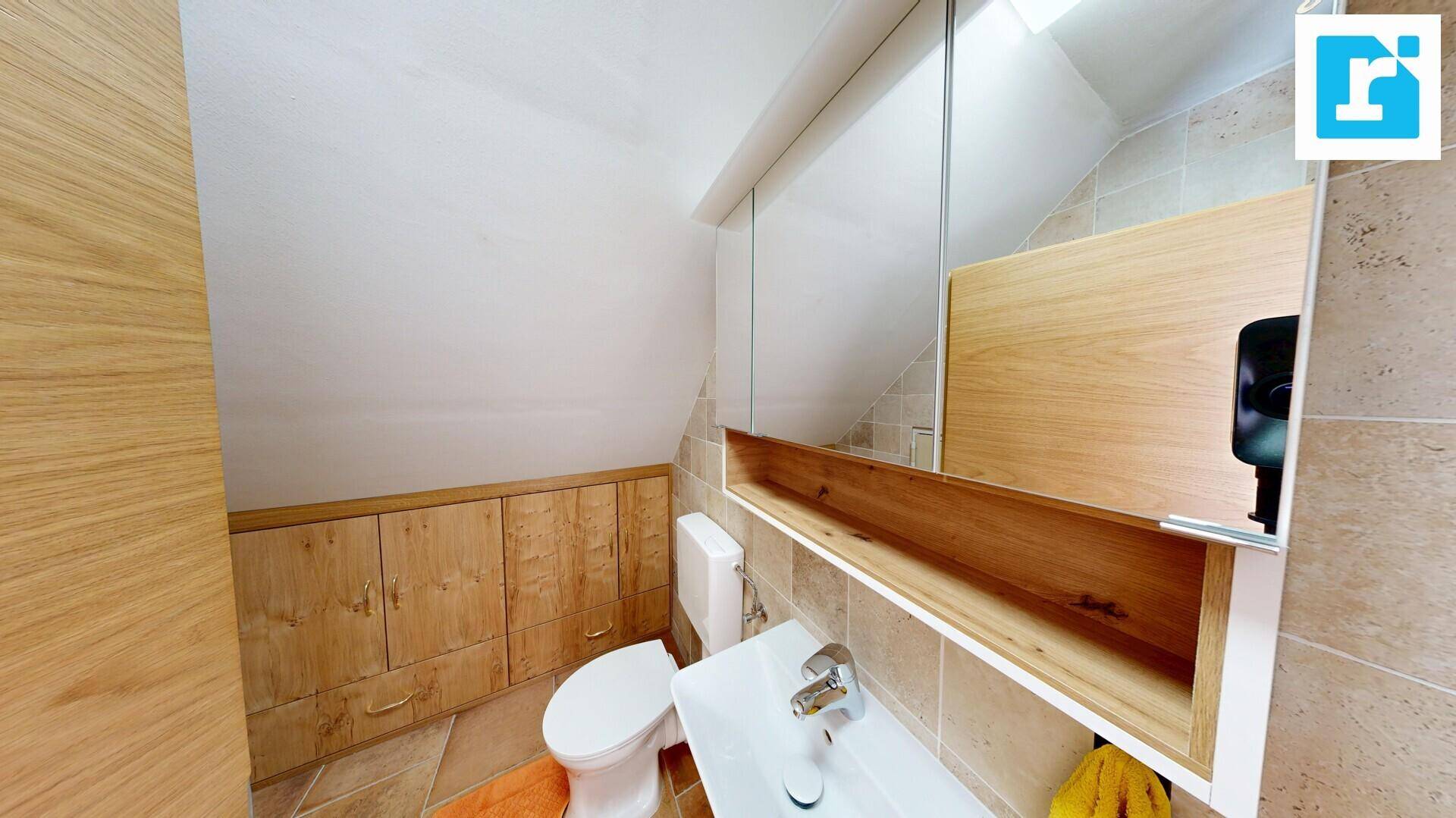 Gemütliches Badezimmer unter Dachschräge mit WC, Waschbecken und Holzschränken.