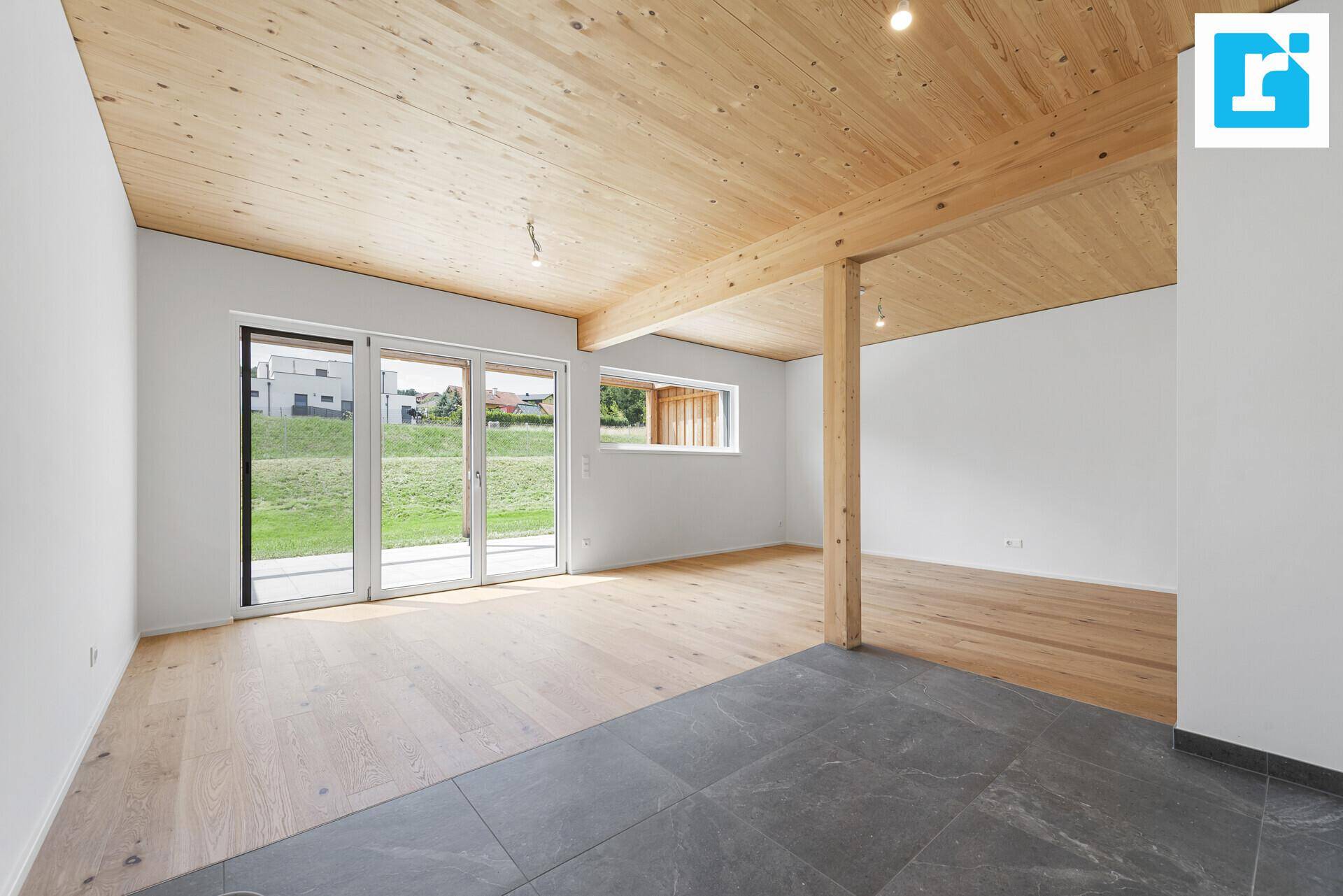 Offener Wohnbereich mit Holzbalkendecke, Parkett- und Fliesenboden sowie Gartenzugang.