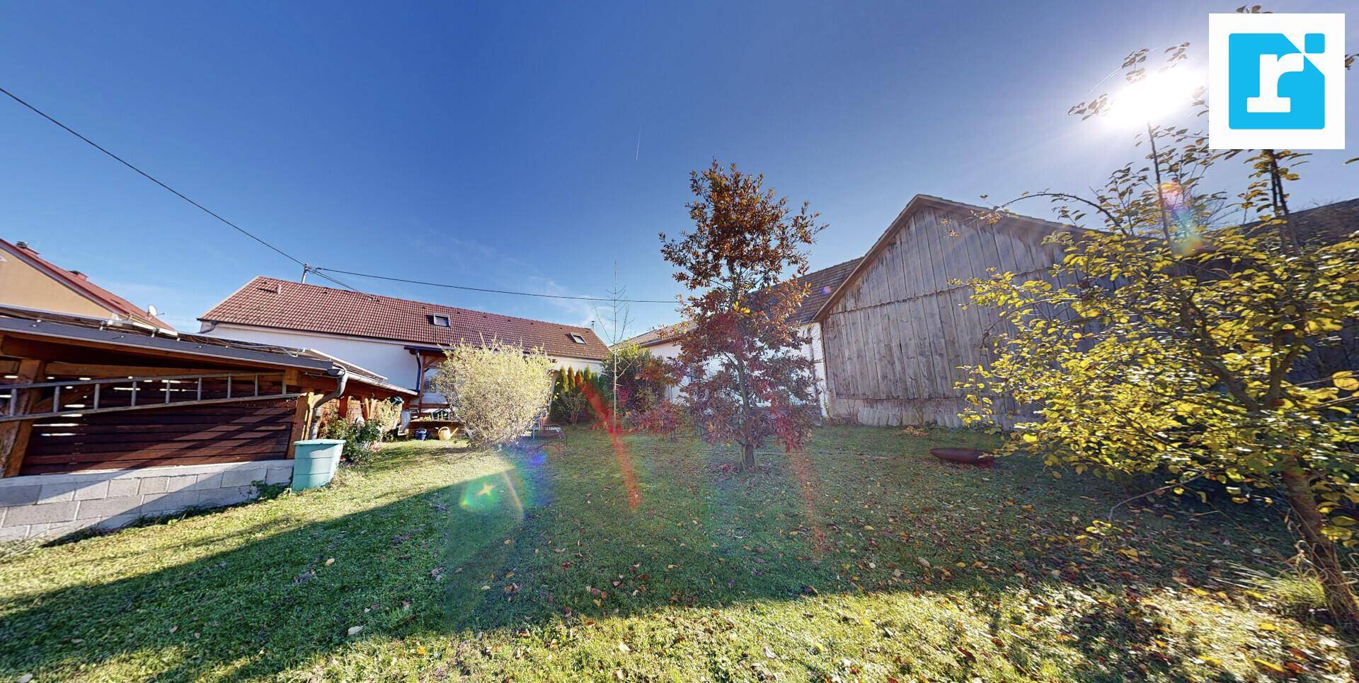 Großer, sonniger Garten mit Rasenfläche, Bäumen und einem Nebengebäude im Hintergrund.