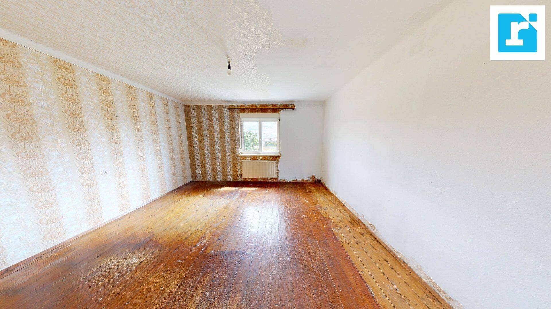 Helles Zimmer mit Holzboden und alter Tapete, bietet Blick ins Grüne.