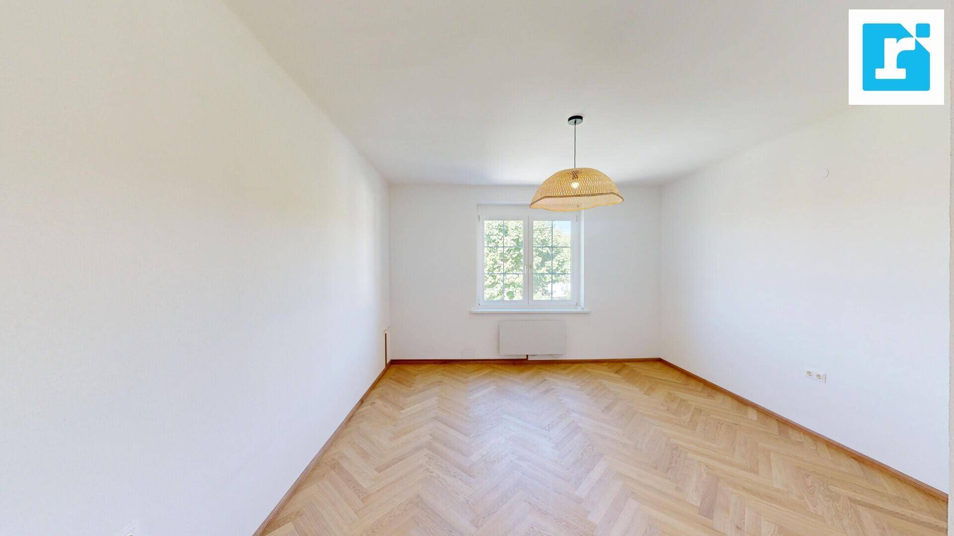 Helles Zimmer mit Fischgrätparkettboden und einem Fenster, das viel Tageslicht hereinlässt.