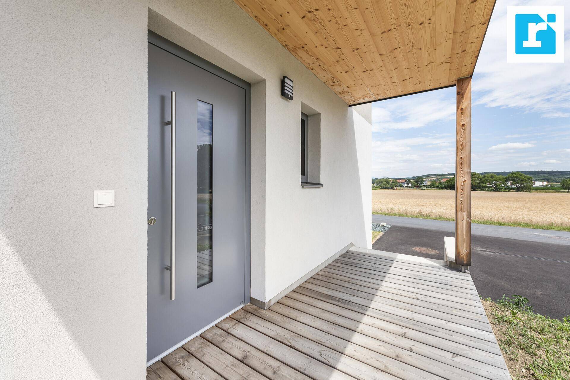 Moderner Eingangsbereich mit grauer Haustür, Holzveranda und Blick ins Grüne.