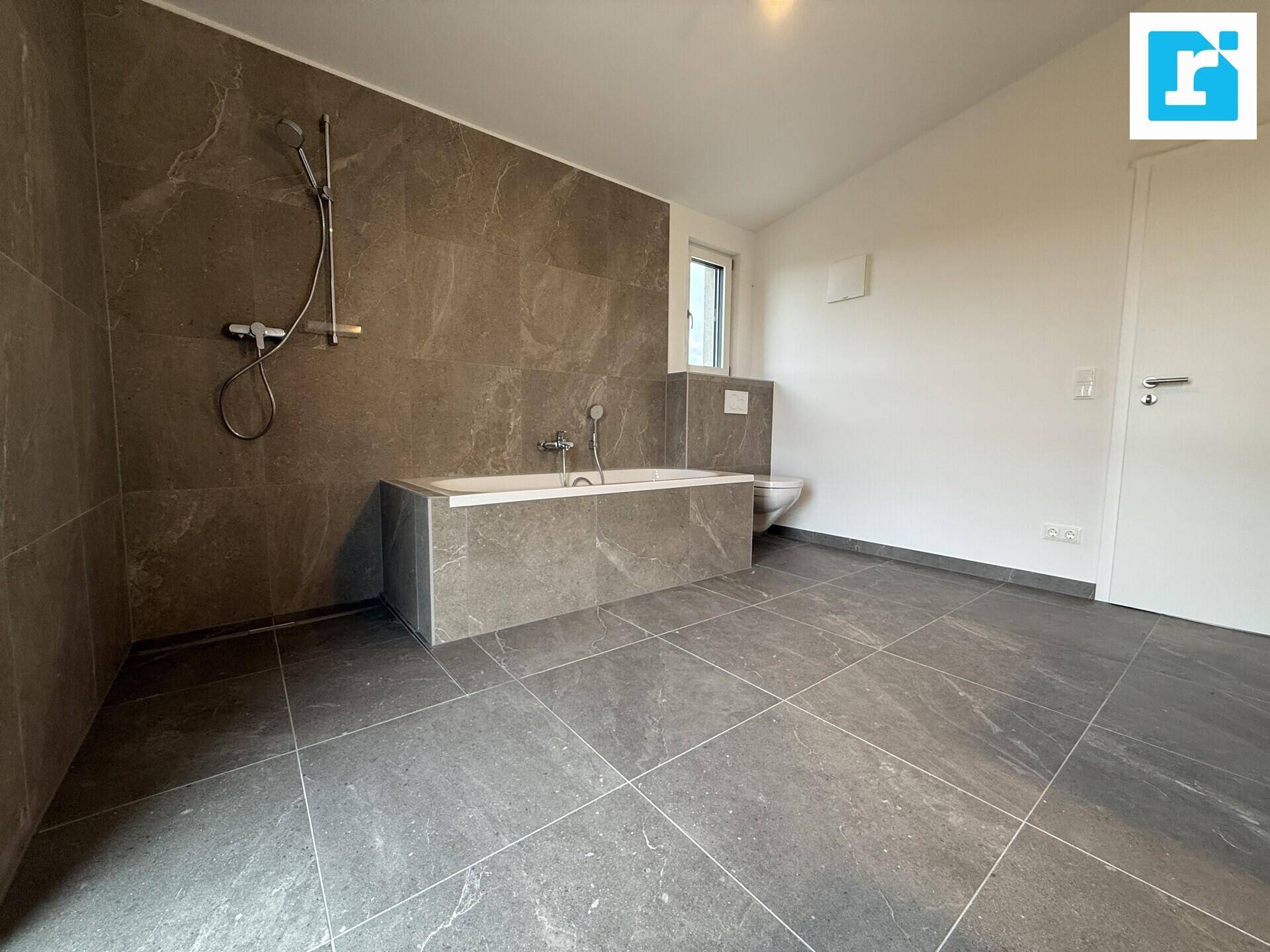 Geräumiges Badezimmer mit Badewanne und modernen grauen Fliesen.