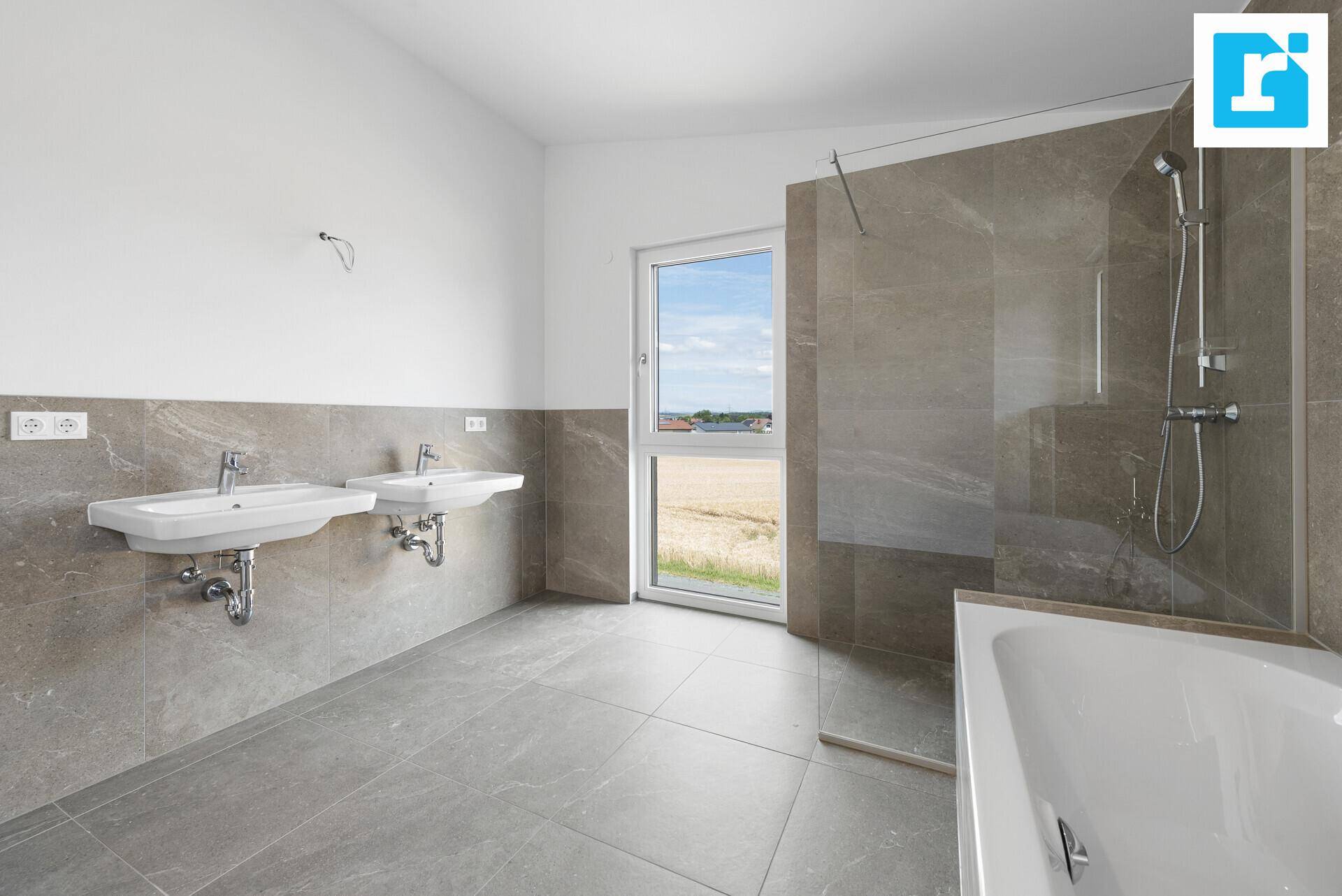 Zeitgemäßes Badezimmer mit Doppelwaschbecken, Dusche und großem Fenster, das viel Licht hereinlässt.