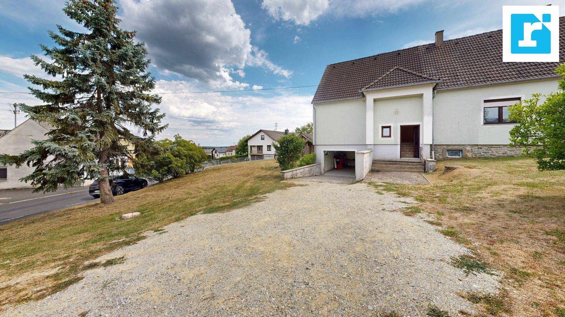 Einfamilienhaus mit Zufahrt, integrierter Garage und umliegender Grünfläche unter blauem Himmel.