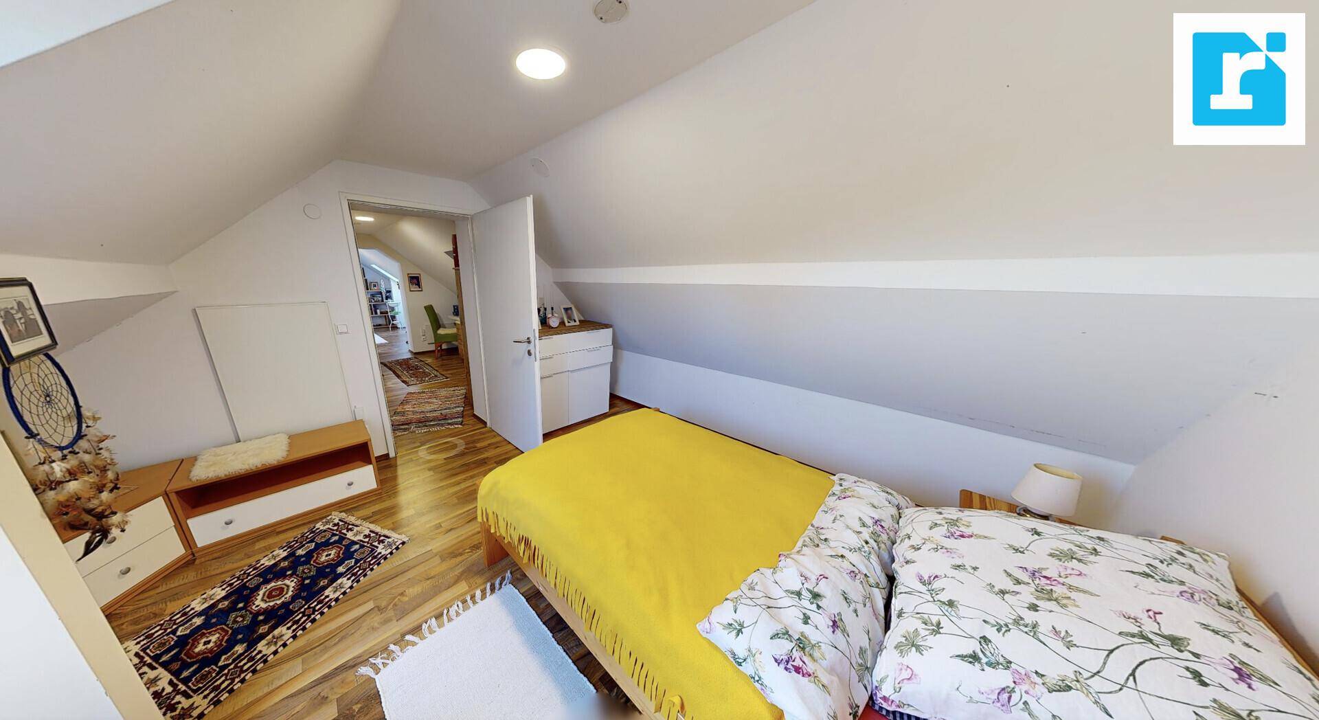 Schlafzimmer im Dachgeschoss mit schrägen Wänden, Holzboden und einem Bett.