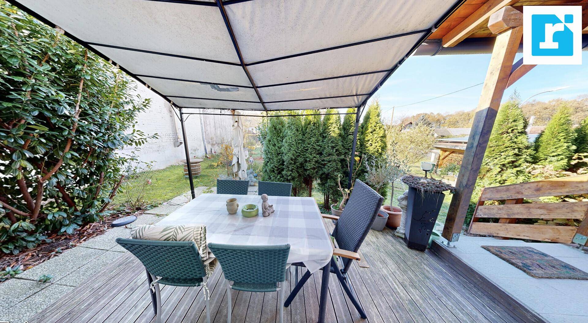 Essbereich im Freien auf einer Holzterrasse, überdacht und von viel Grün umgeben.