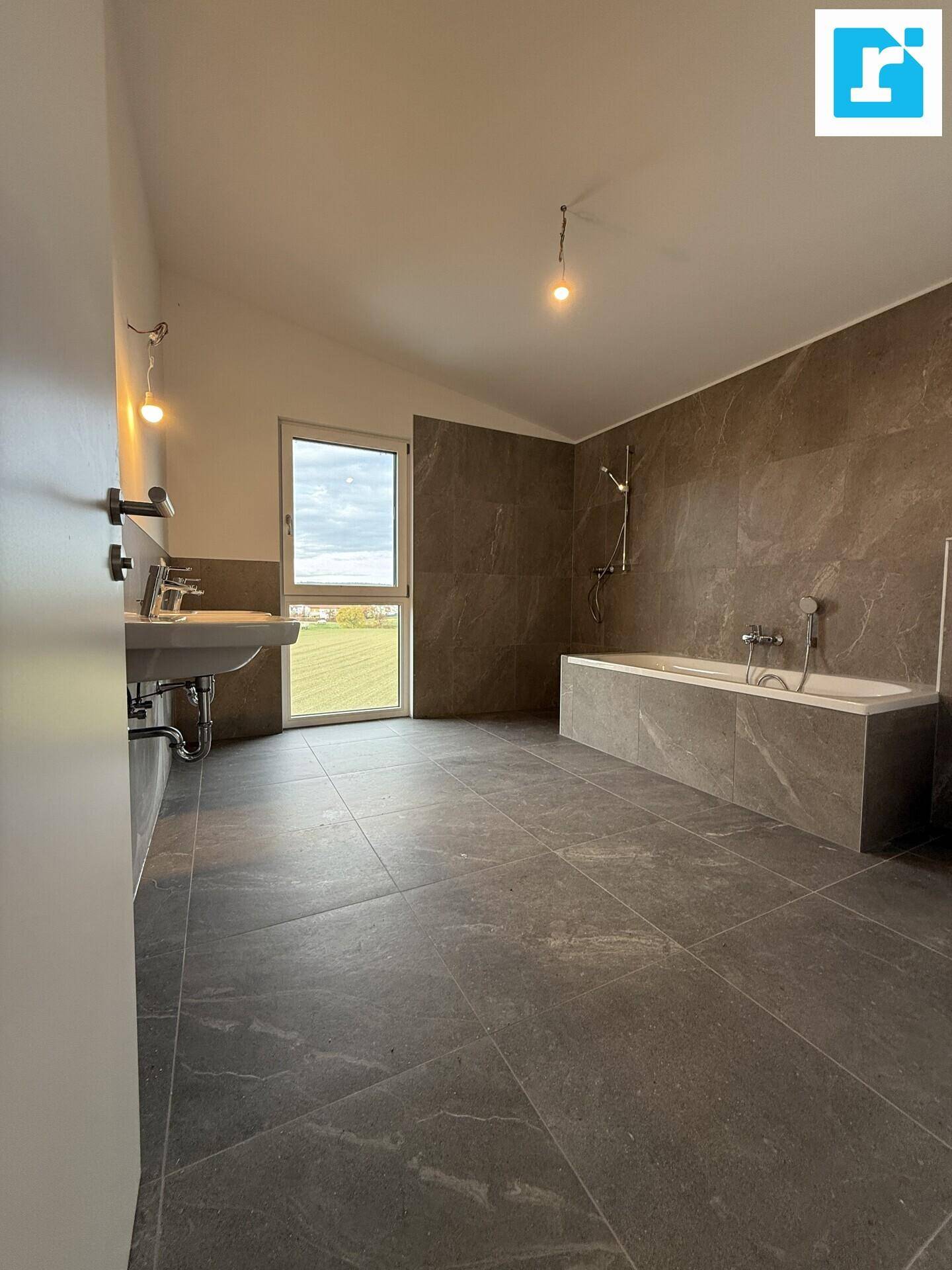 Großes Badezimmer mit Badewanne, Waschbecken und Fenster mit Ausblick.