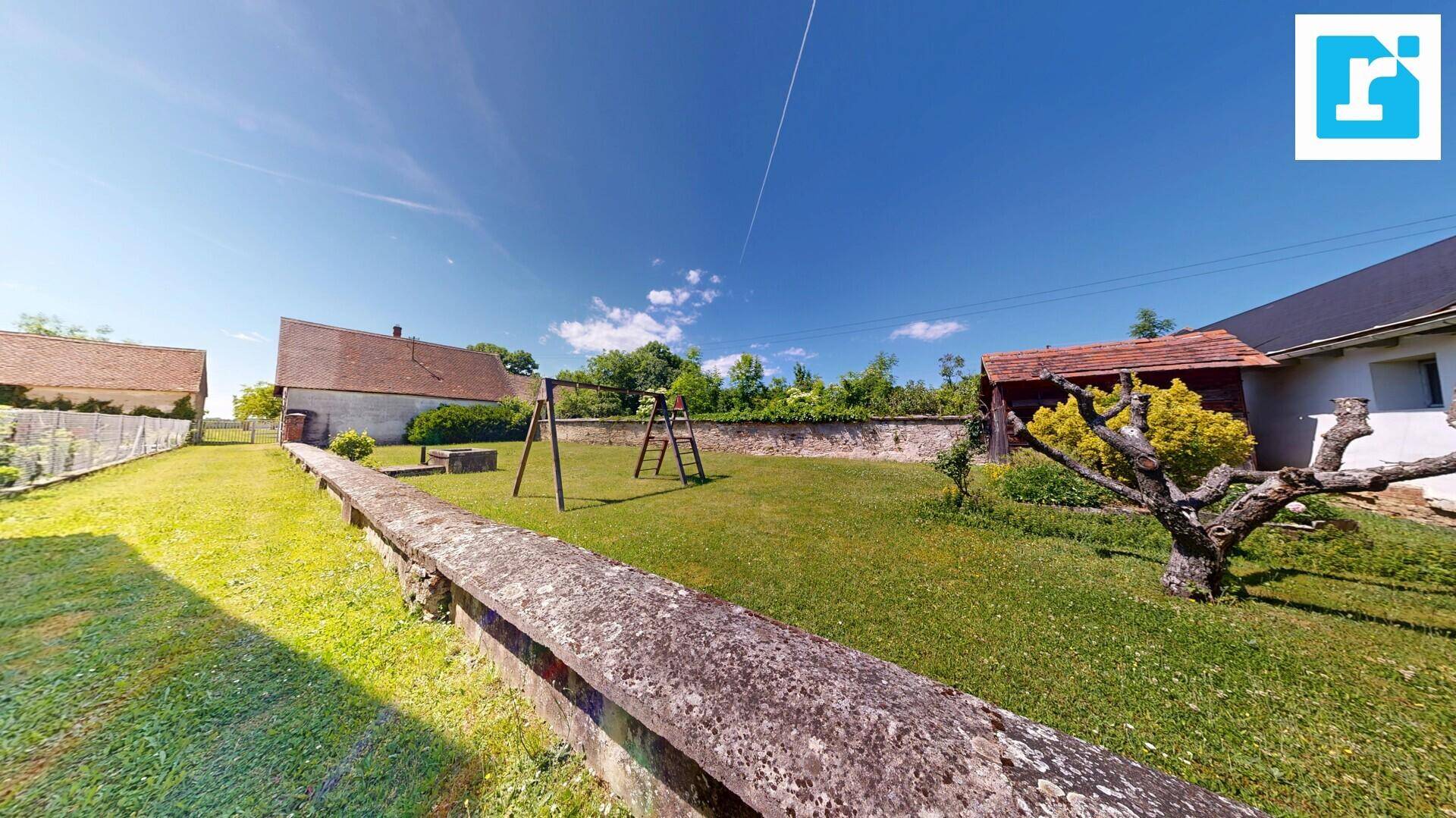 Großer Garten mit Rasenfläche, Schaukel und alten Steinmauern unter blauem Himmel.